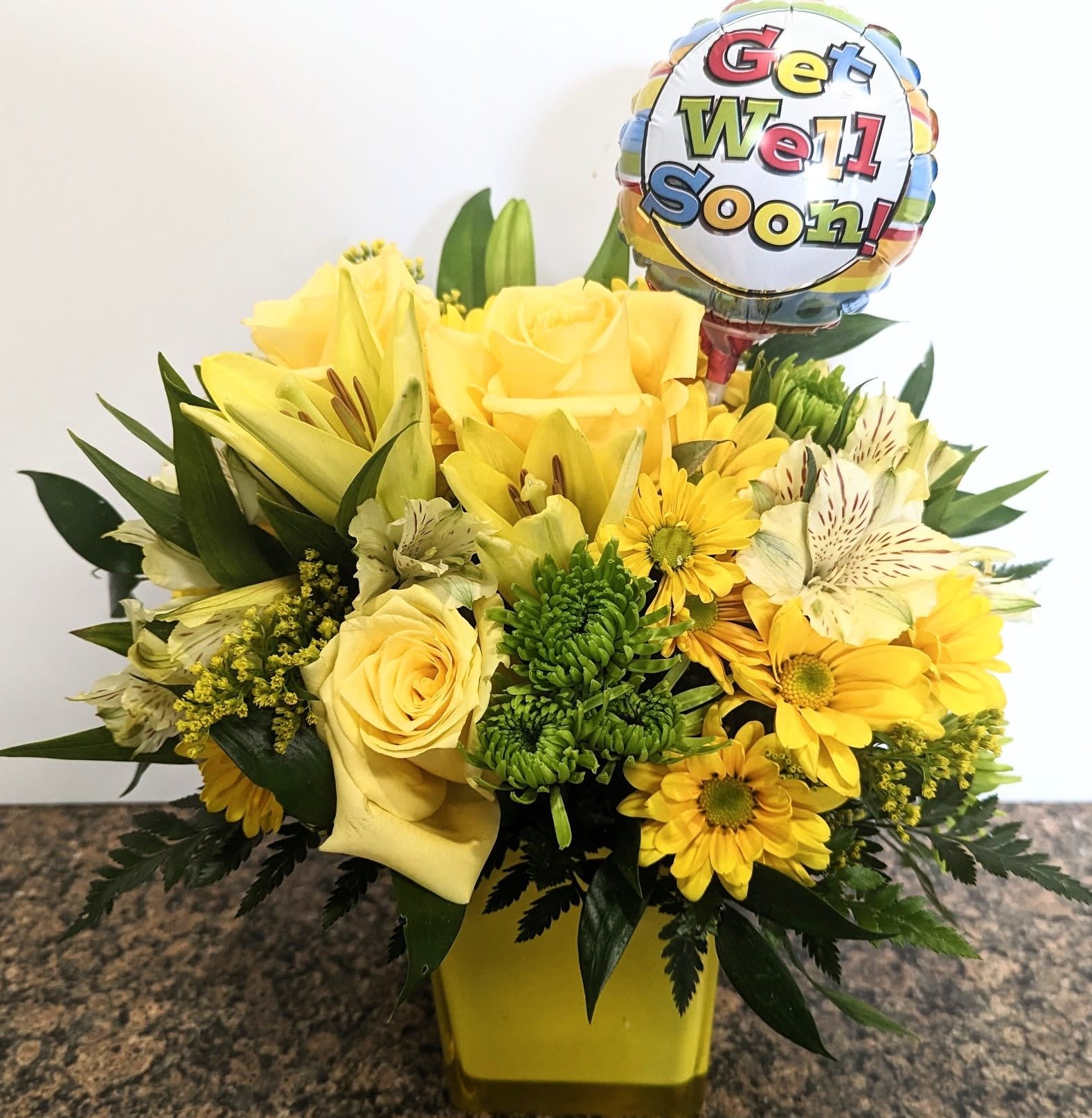 Yellow flower arrangement with a get well soon balloon in a vase