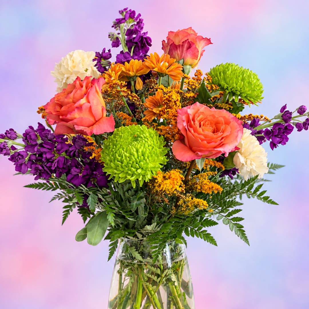 Colorful mixed bouquet in a clear glass vase with roses, chrysanthemums, and purple blooms