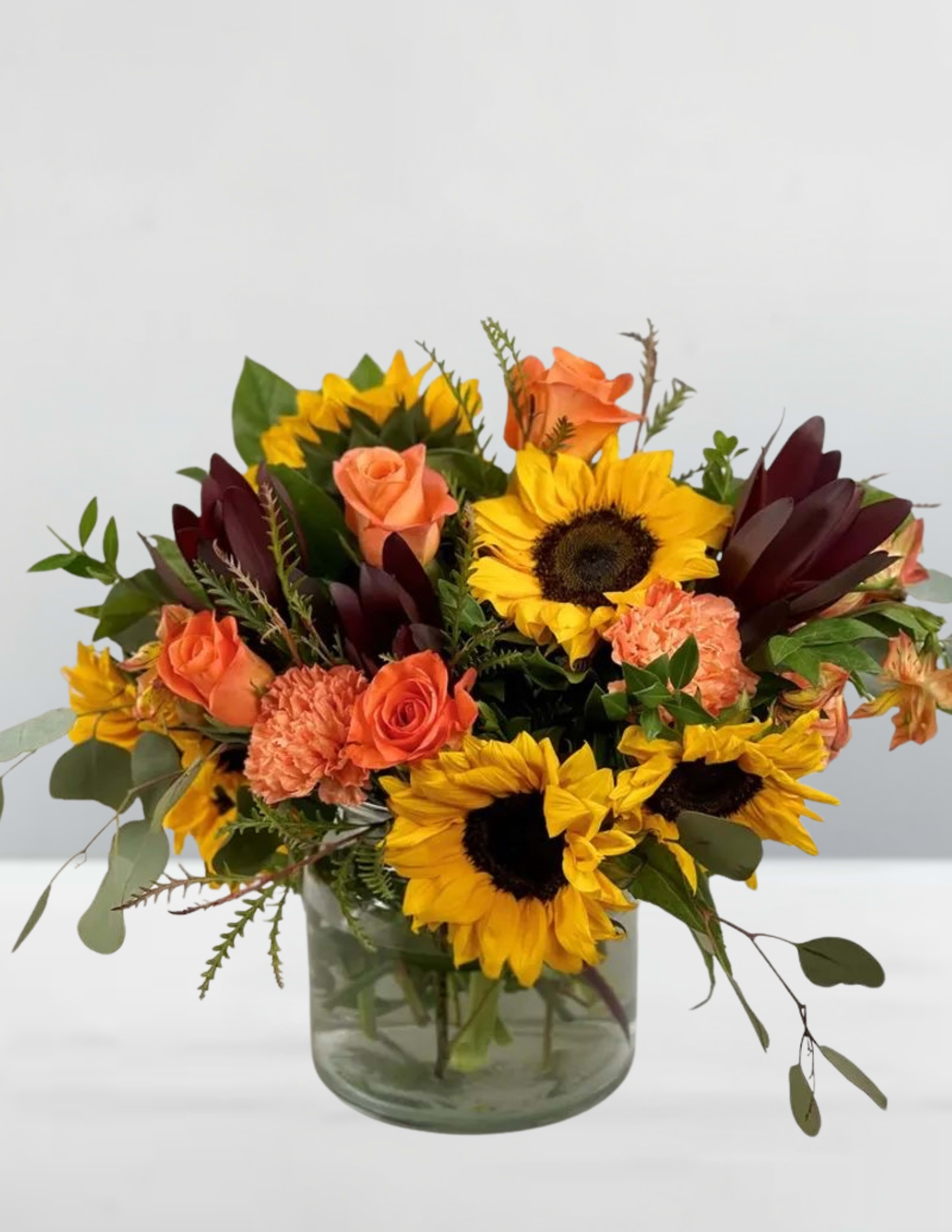 Bouquet of sunflowers, orange roses, and carnations in a glass vase