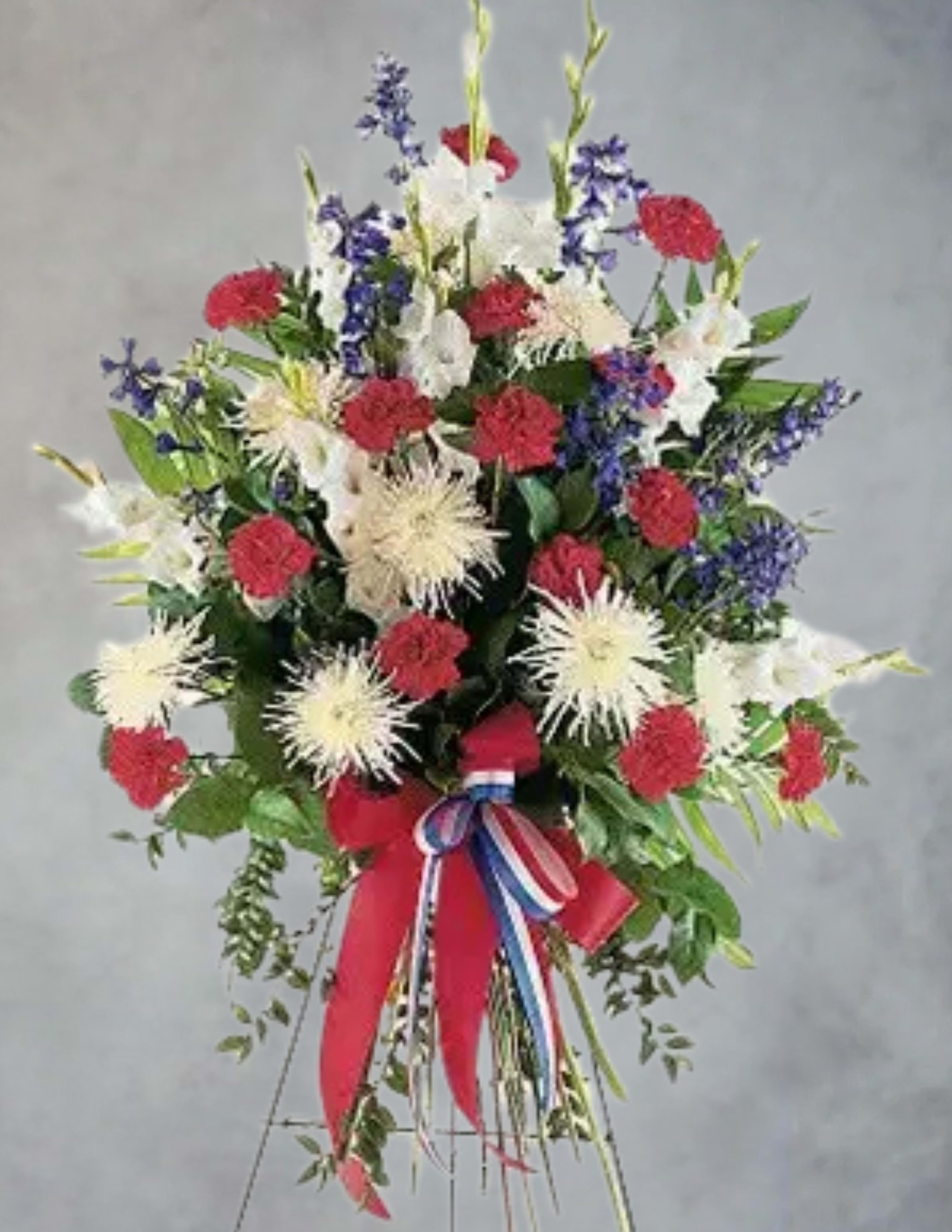 Blessed Patriot standing spray - The Blessed Patriot Spray is composed of traditional red, white, and blue blooms and is presented on an easel to allow for a traditional ceremonial or graveside tribute.
