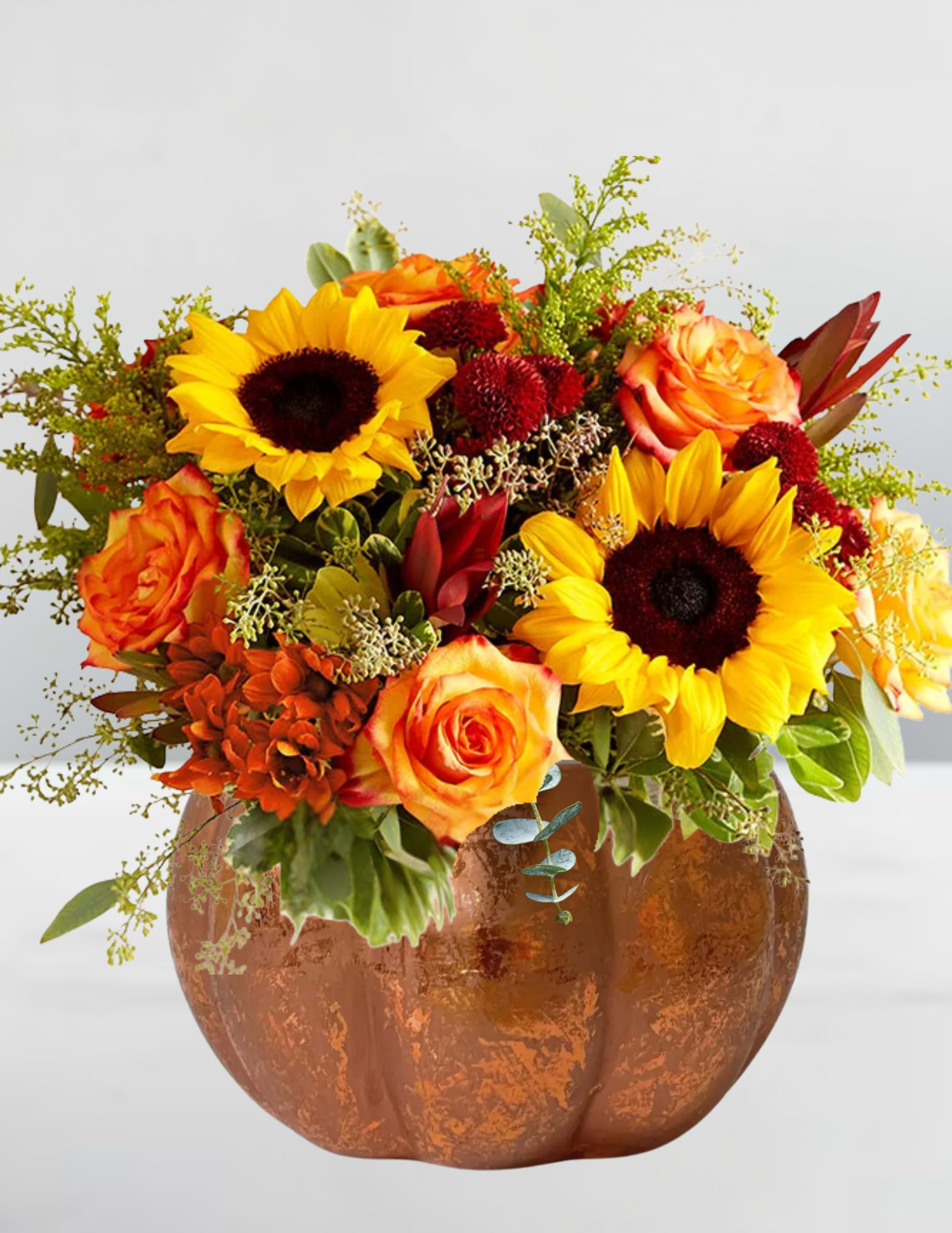 Orange roses and sunflowers arranged in a copper pumpkin vase