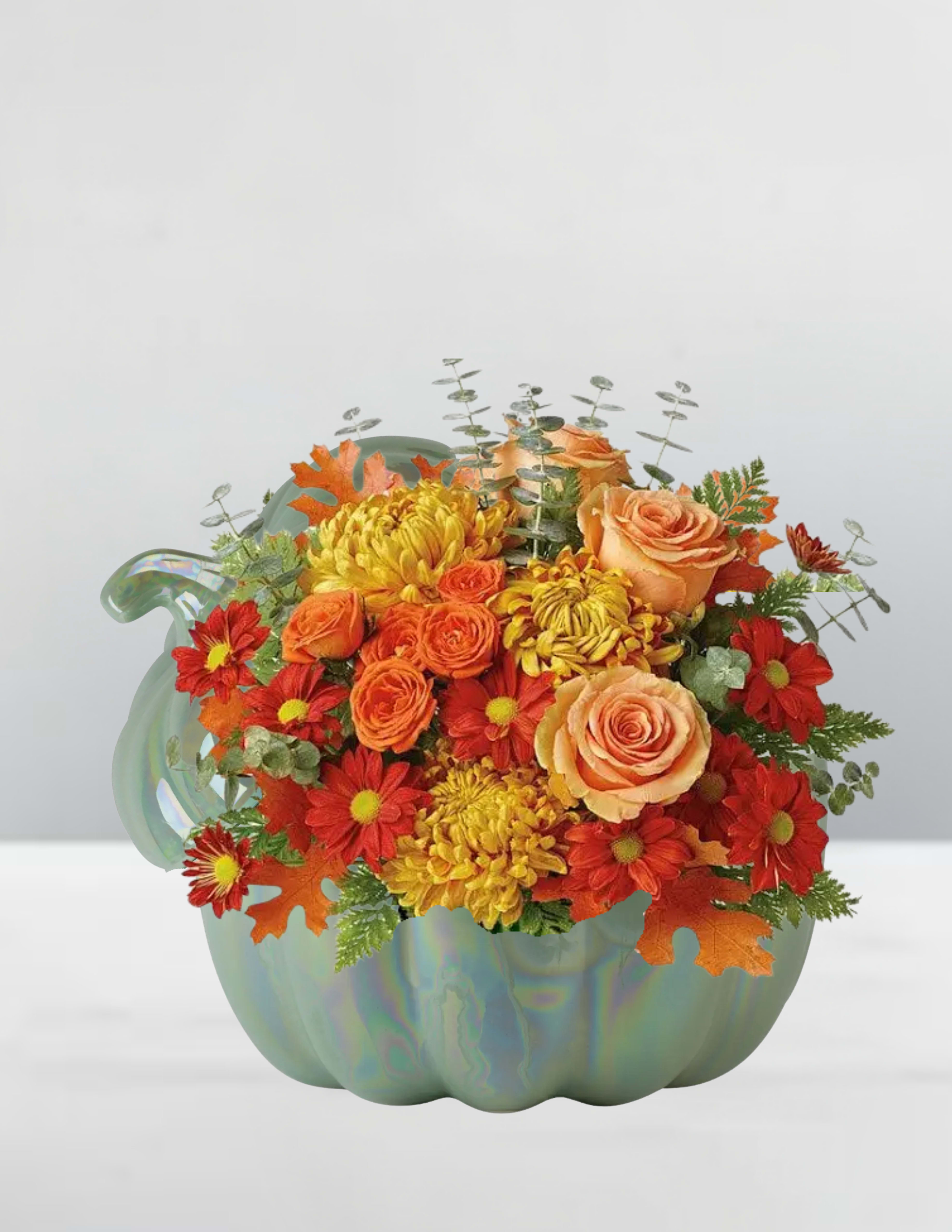 Autumn Glow Pumpkin Arrangement - Bring the golden warmth of fall indoors with our Autumn Glow Pumpkin Arrangement. Designed in a charming iridescent teal pumpkin vase, this bouquet features lush peach roses, vibrant orange spray roses, golden mums, and rich red daisy poms. Accented with airy eucalyptus and festive autumn leaves, this design radiates cozy harvest charm. Perfect for a Thanksgiving centerpiece, seasonal gift, or to brighten your own home, it’s a celebration of autumn’s beauty in full color.