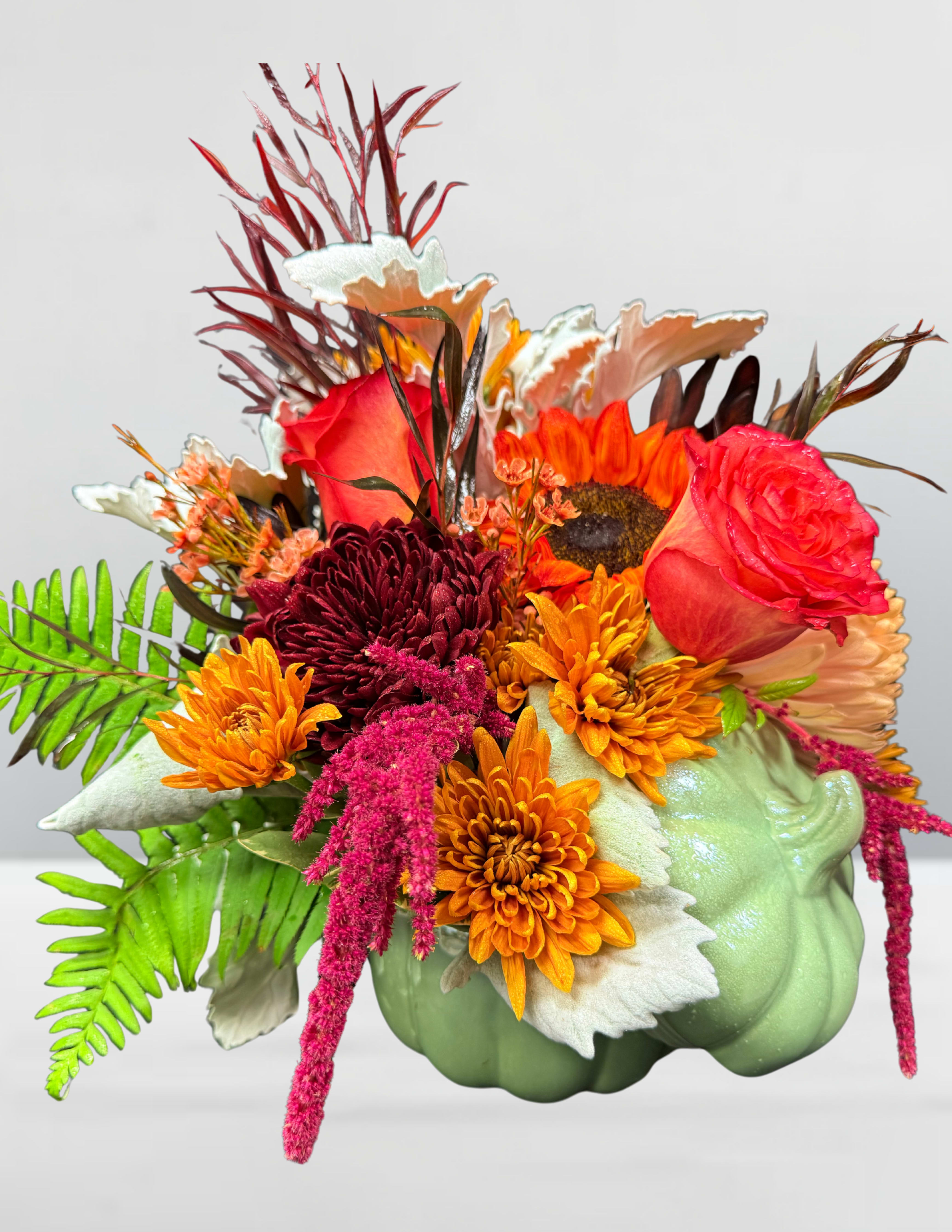 Sunset &amp; spice - Sunset &amp; Spice A bouquet steeped in autumn’s glow—where fiery chrysanthemums meet the golden gaze of sunflowers, and crimson roses smolder like embers at dusk. Wisps of white foliage and fern add contrast and movement, while a pale green pumpkin nestles in like a whispered secret of harvest. This arrangement is a sensory stroll through falling leaves, spiced cider, and the last light of day—perfect for cozy gatherings, Thanksgiving tables, or anyone craving a touch of seasonal romance.