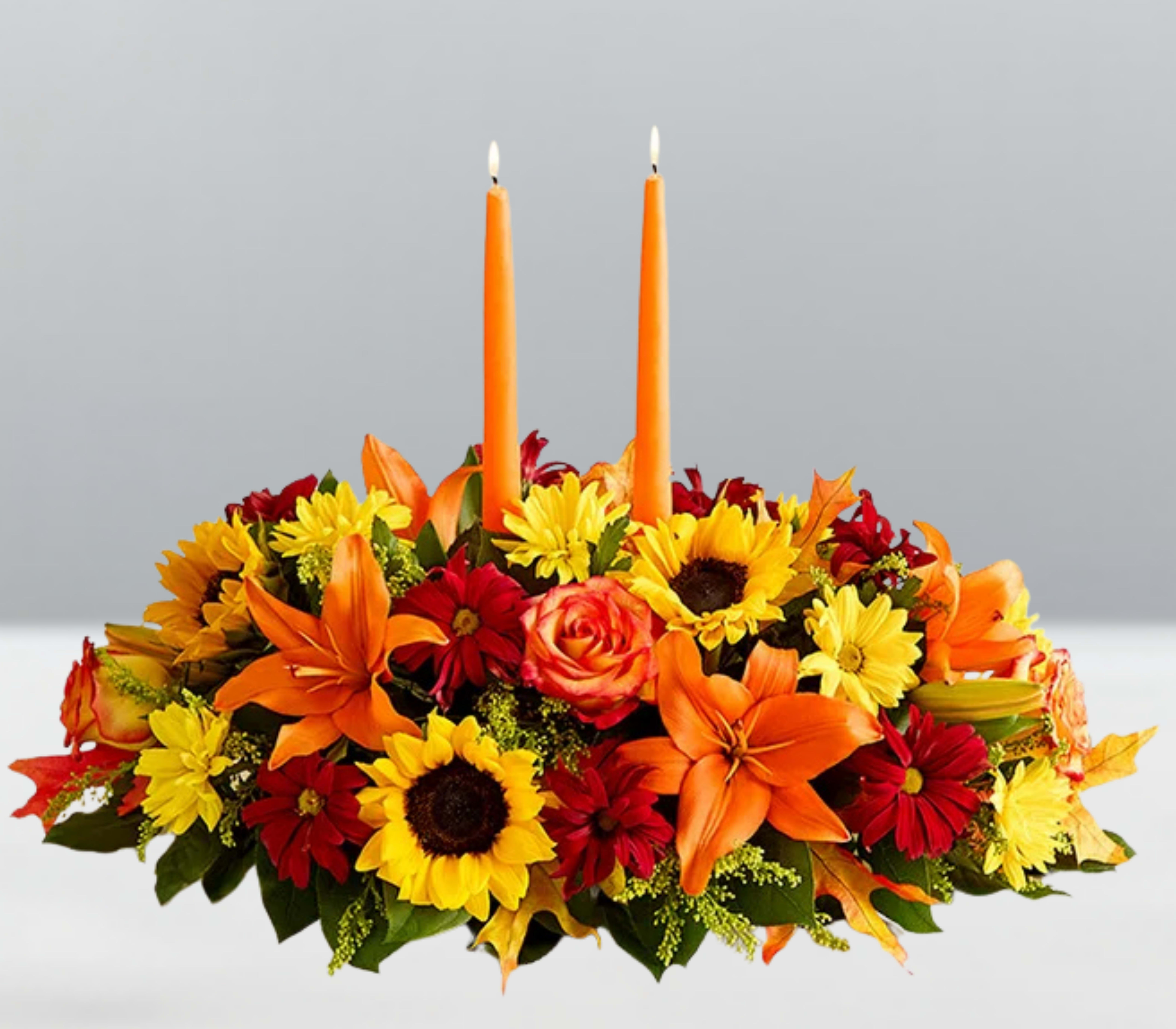 Thanks &amp; twinkles -  Thanks &amp; Twinkles  A joyful nod to the season of gratitude—Thanks &amp; Twinkles features glowing taper candles nestled among sunflowers, orange lilies, golden mums, and radiant roses. Accented with berries and lush greenery, this arrangement sparkles with warmth and whimsy. It’s a celebration of togetherness, designed to light up your table with beauty, brightness, and heartfelt thanks.