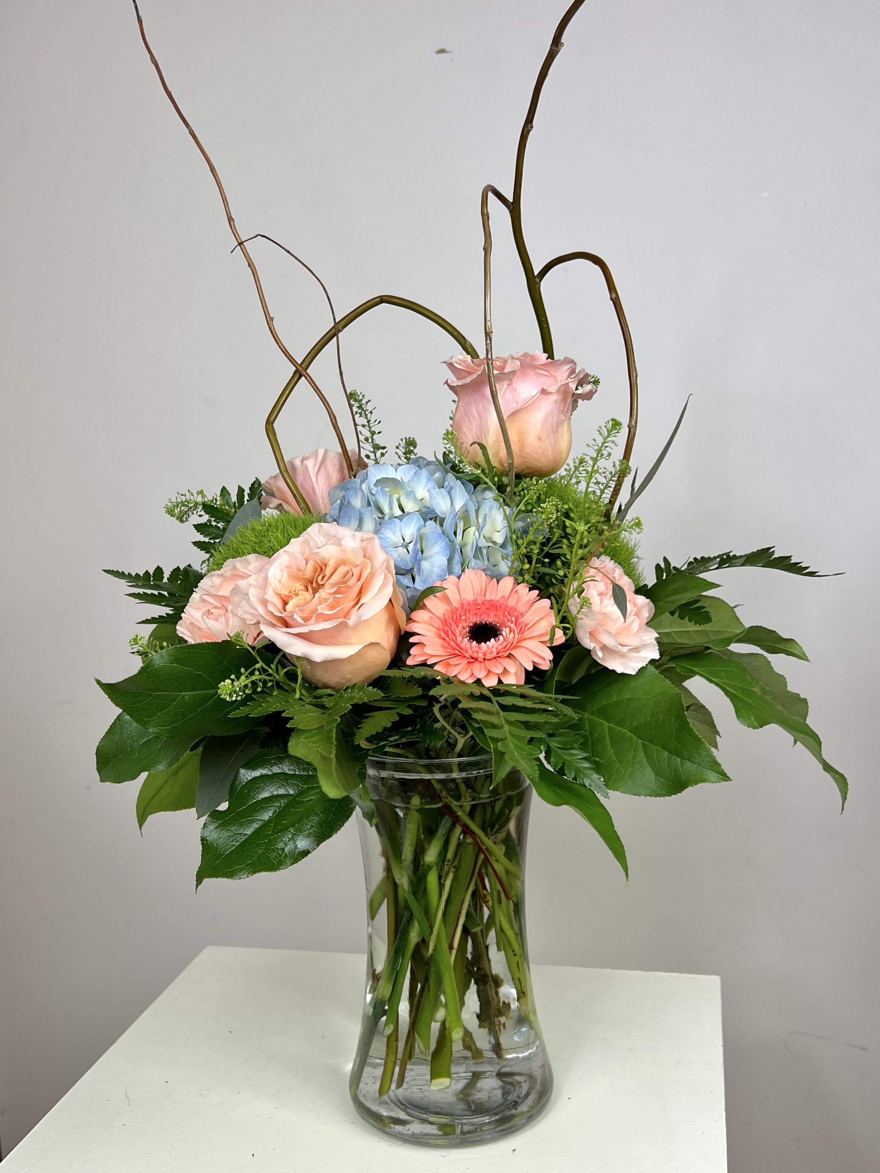 Pink roses and a blue hydrangea in a clear glass vase