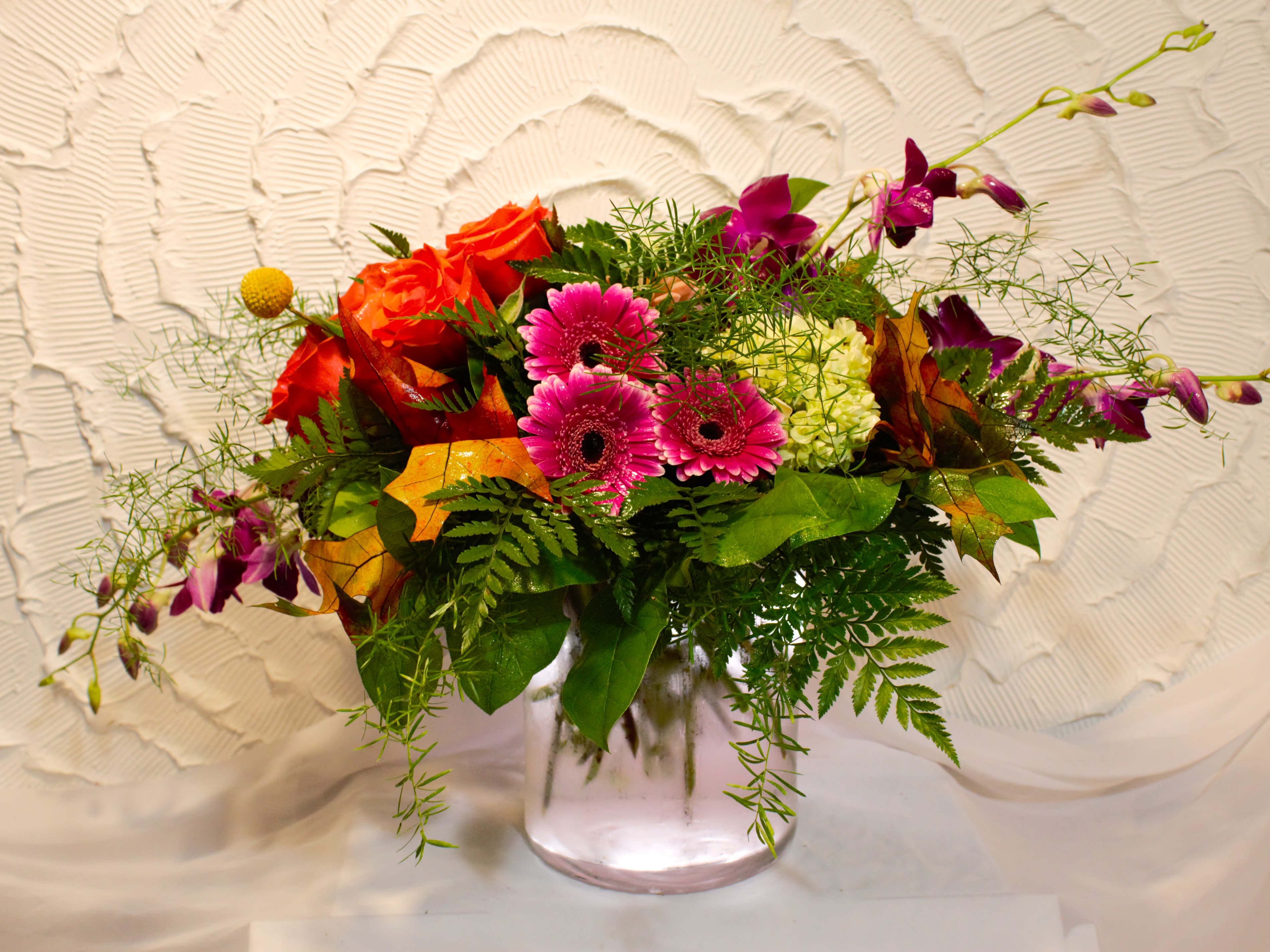 Mixed bouquet of orange roses, pink gerberas, and purple orchids in a glass vase
