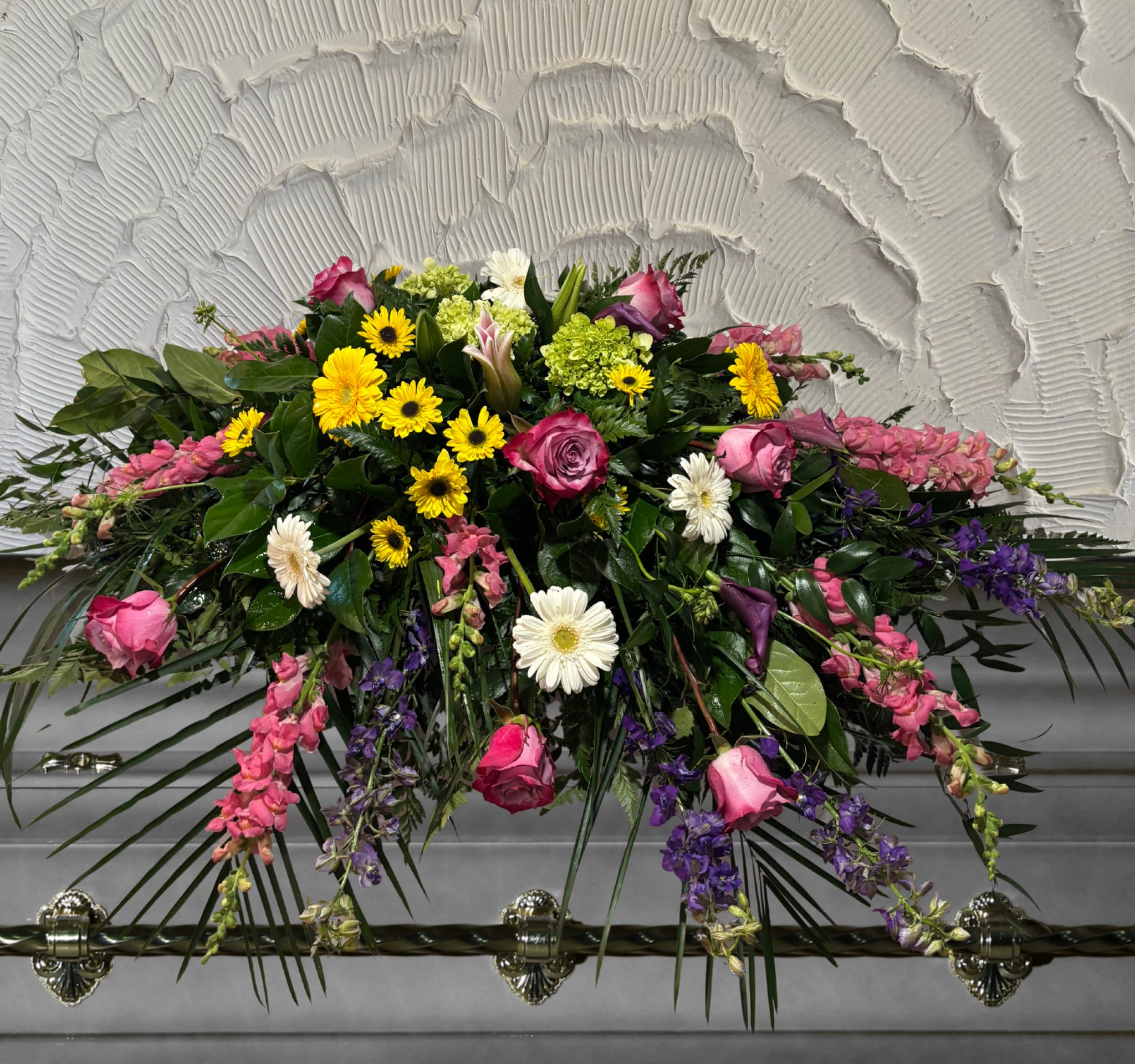 Casket spray with pink roses, yellow daisies, and purple flowers