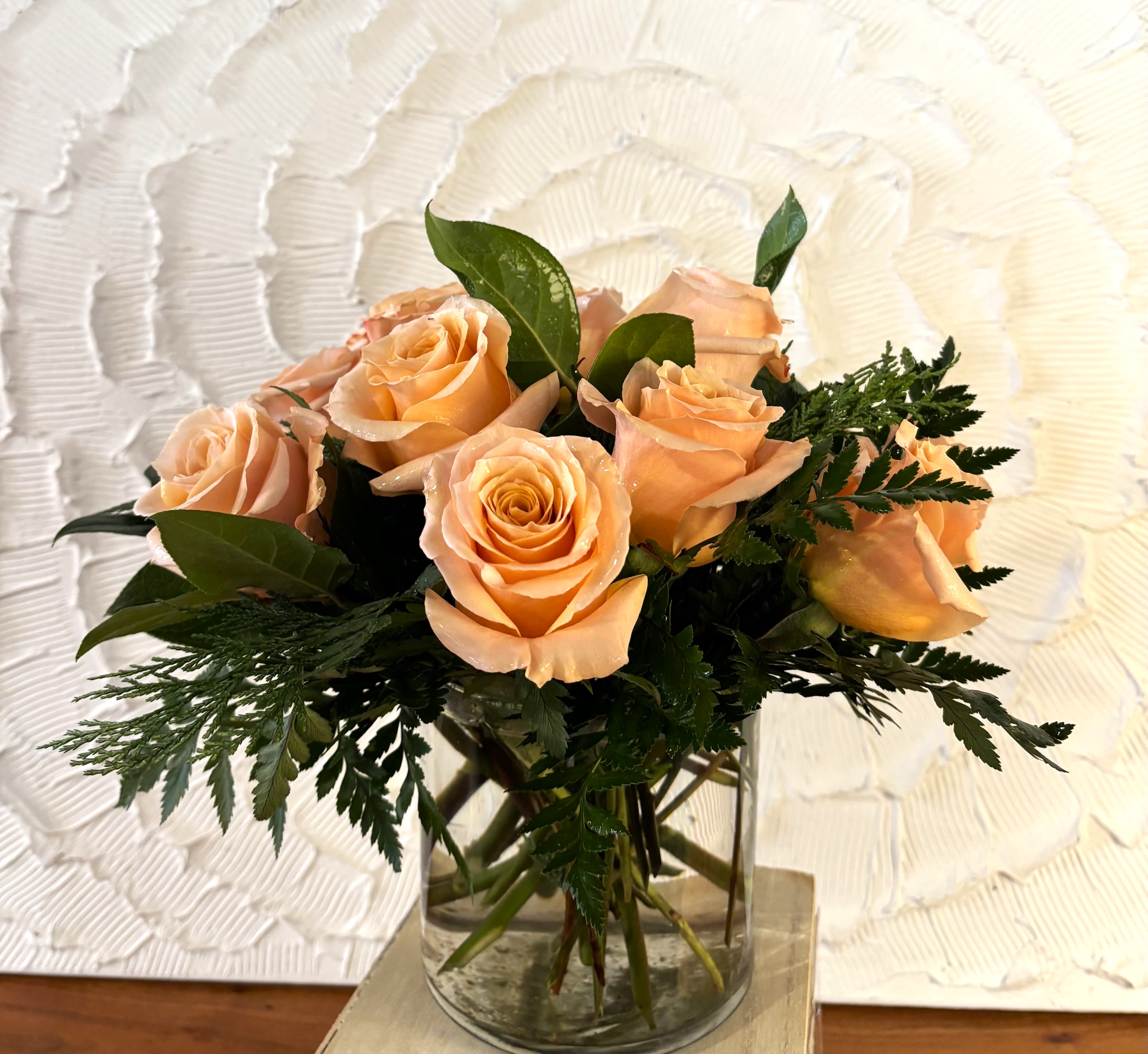 Peach roses arranged in a clear glass vase with greenery