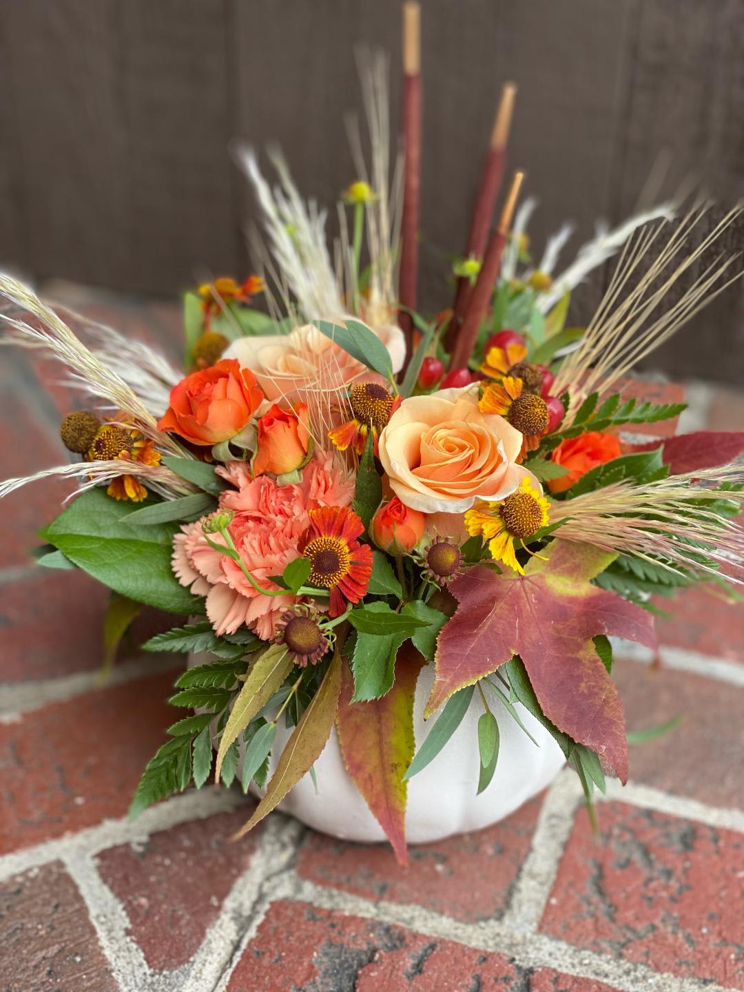 Orange and peach roses in a white vase with autumn flowers