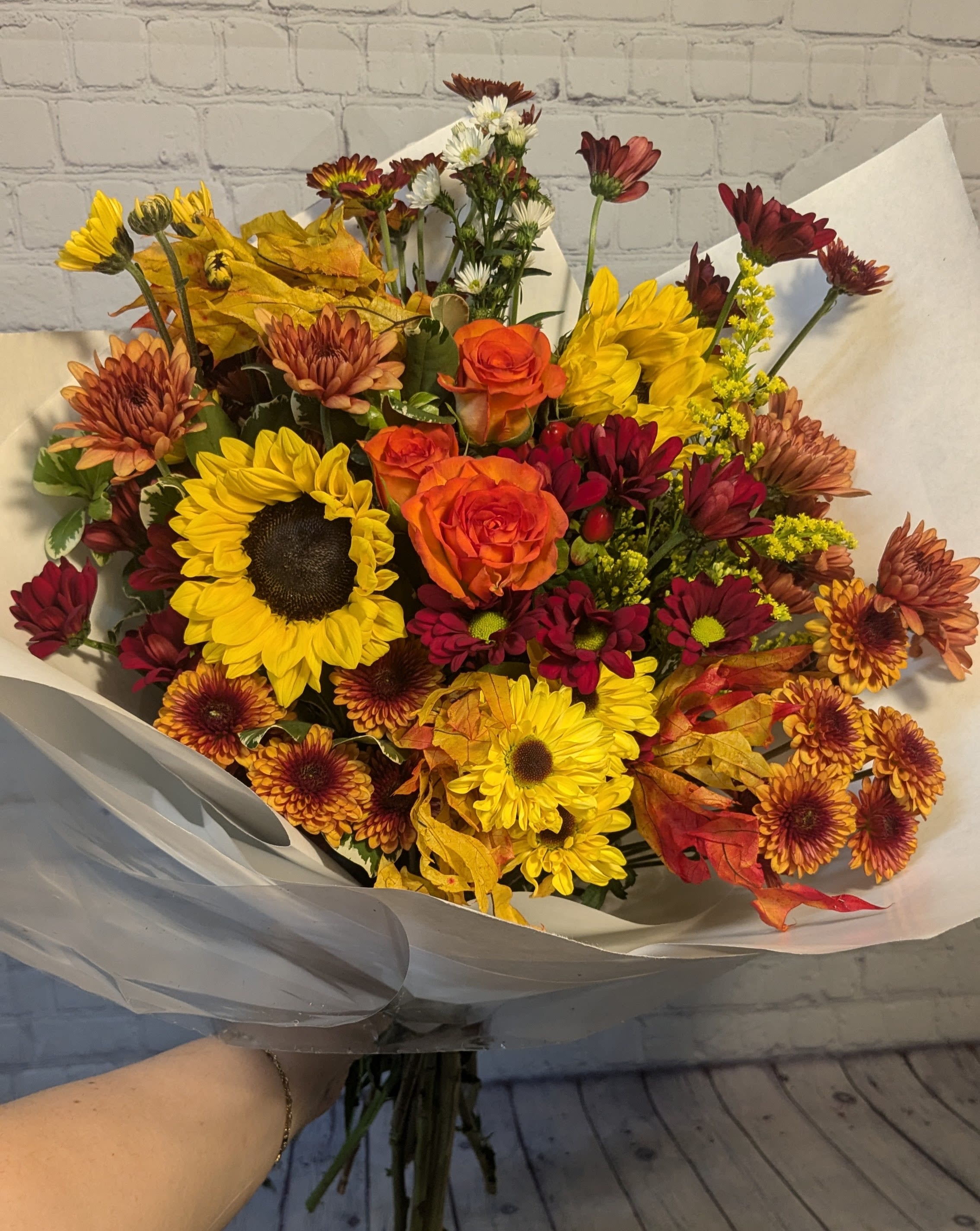 Hello Fall Hand-tied Bouquet - Say, "Hello to Fall" with our favorite seasonal hand-tied bouquet. This bouquet features a mix of autumn colored chrysanthemum cushions &amp; daisies, spray roses, sunflowers, hypericum, monte, solidago, and glycerin leaves.  This is a hand-tied bouquet, not a vase arrangement. 