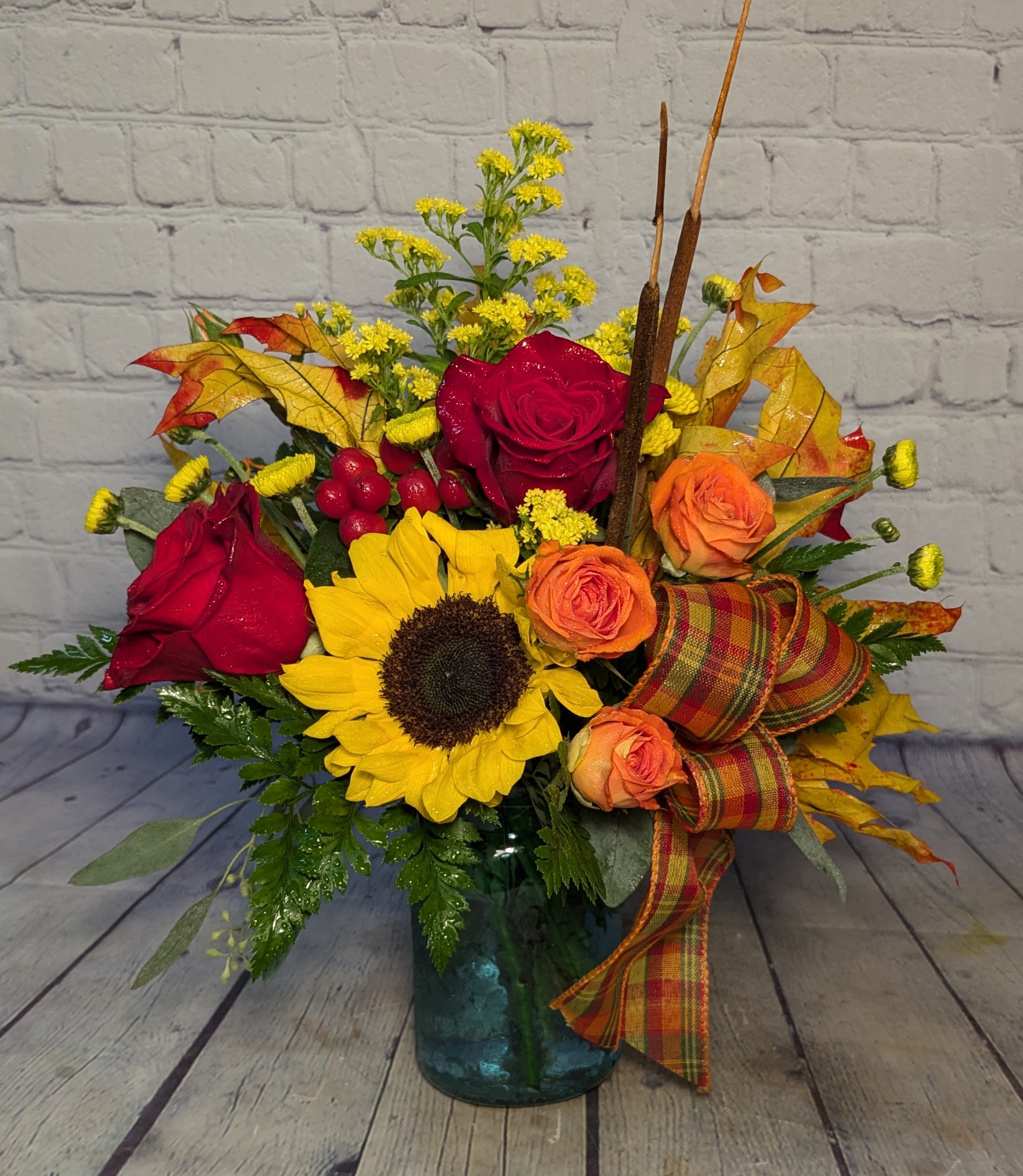Emerald Eve - This bouquet puts a spin on the everyday autumn style with a deep emerald vase that brightens the yellows and oranges of the season. Say hello to autumn with gorgeous sunflowers, spray roses, hypernicum berries, and real fall leaves. 