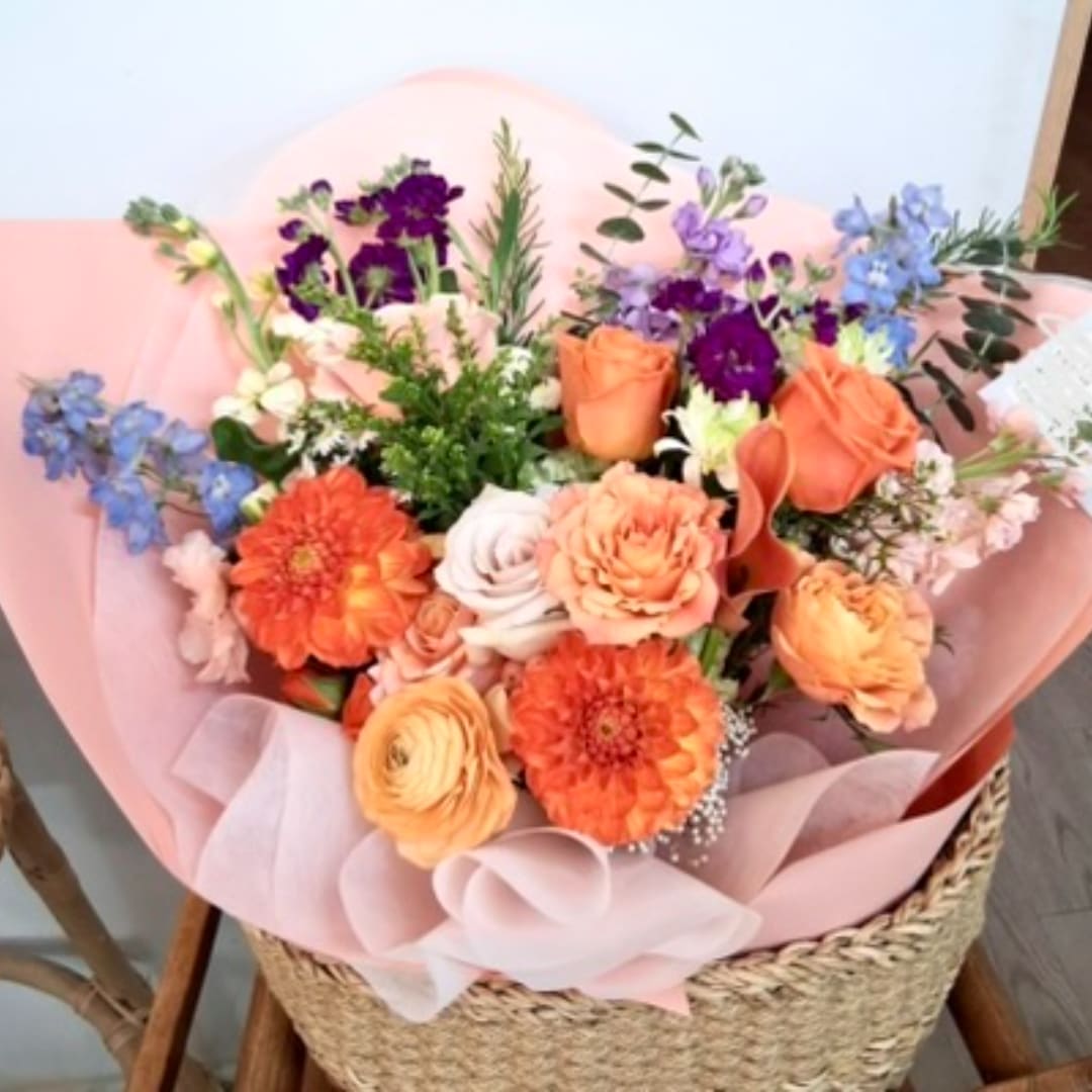 Mixed bouquet of orange, purple, and blue flowers wrapped in pink paper