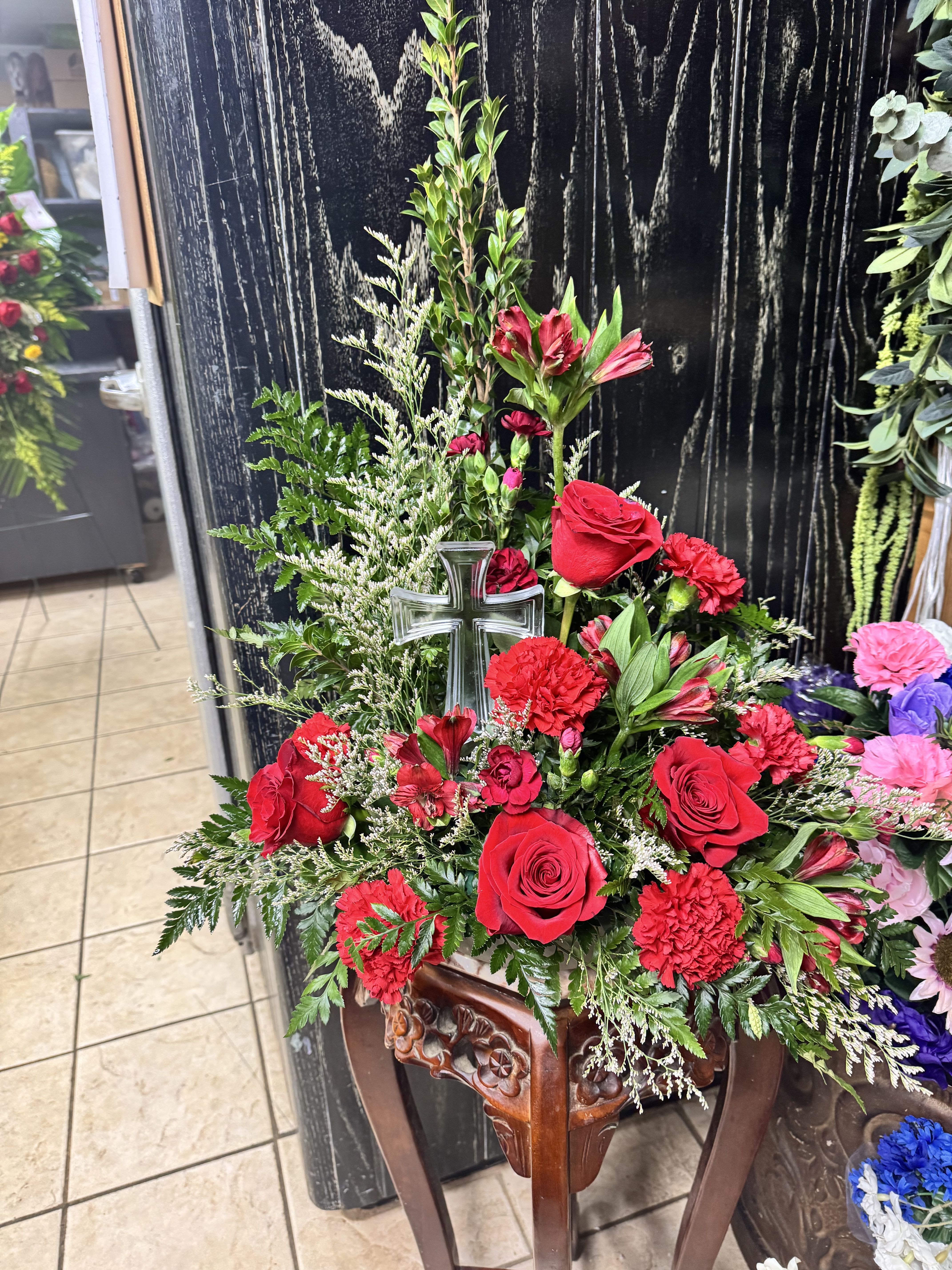 Red roses and carnations arranged with a glass cross in a wooden stand
