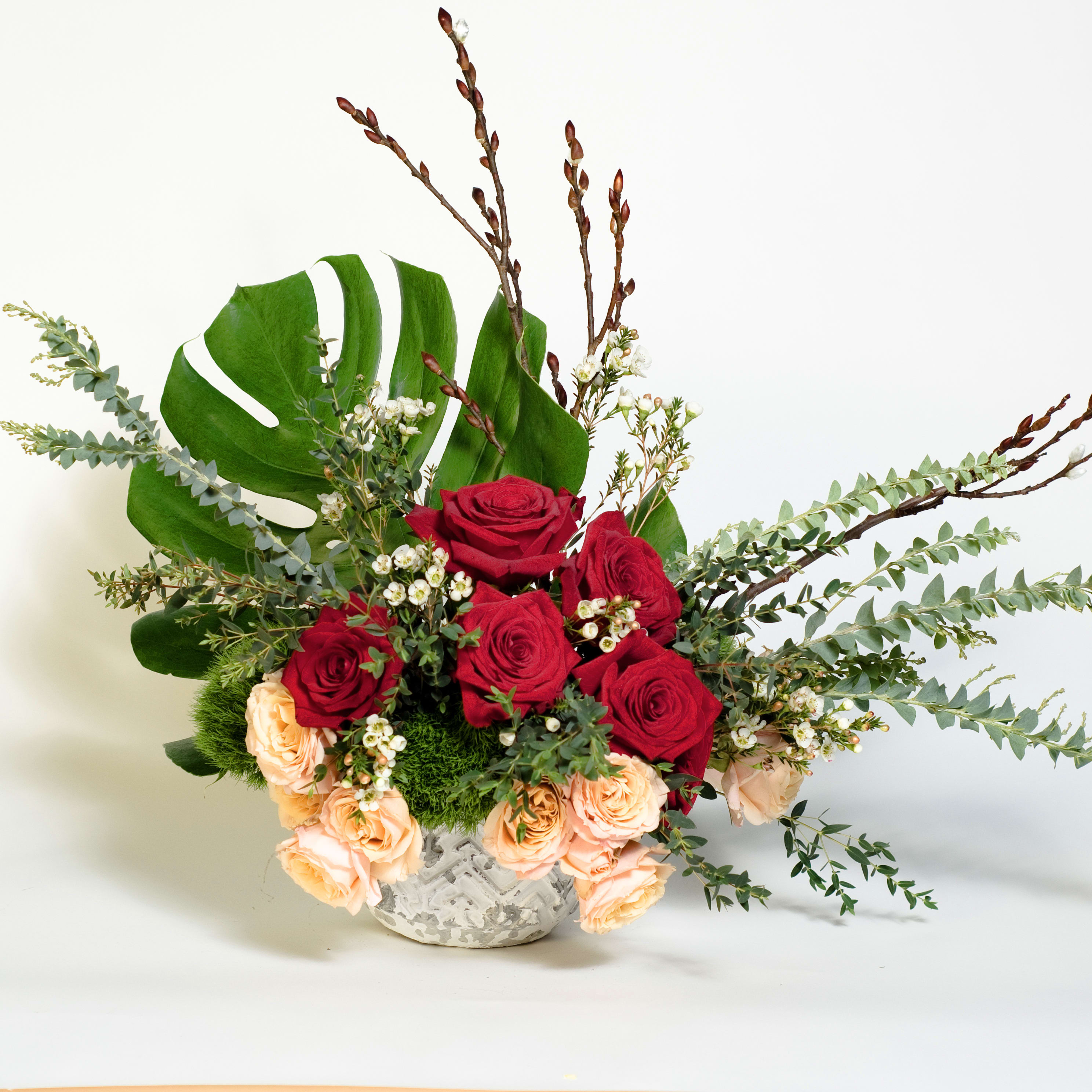 Brie - a dozen of roses, combination of red and pastel, arranged in white ceramic vase. A low compact arrangement is accented with a large green leaf and twigs. (Approx. Size 16"w x 10"d x 18"h)