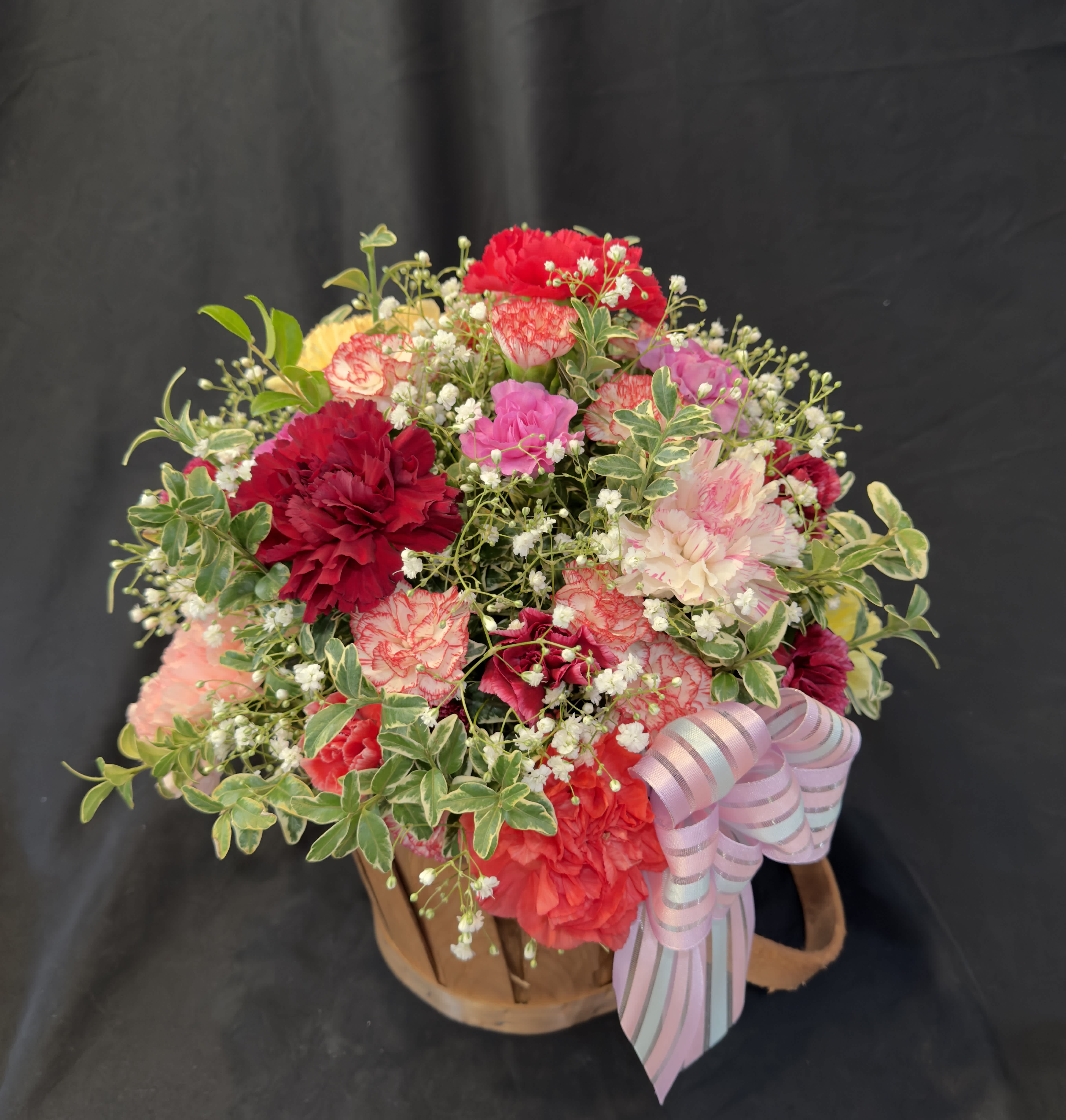Mixed bouquet of red, pink, and white carnations in a basket with a ribbon