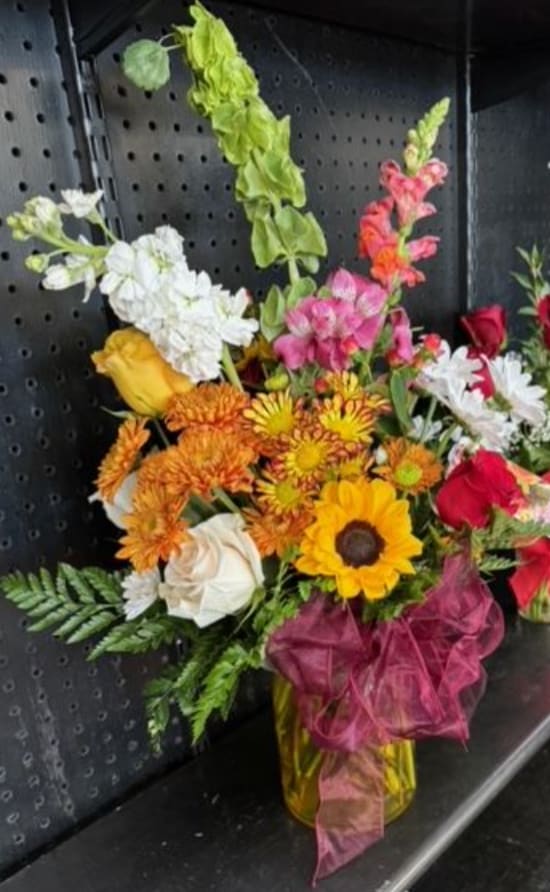 Mixed bouquet in a yellow vase with sunflowers, roses, and snapdragons