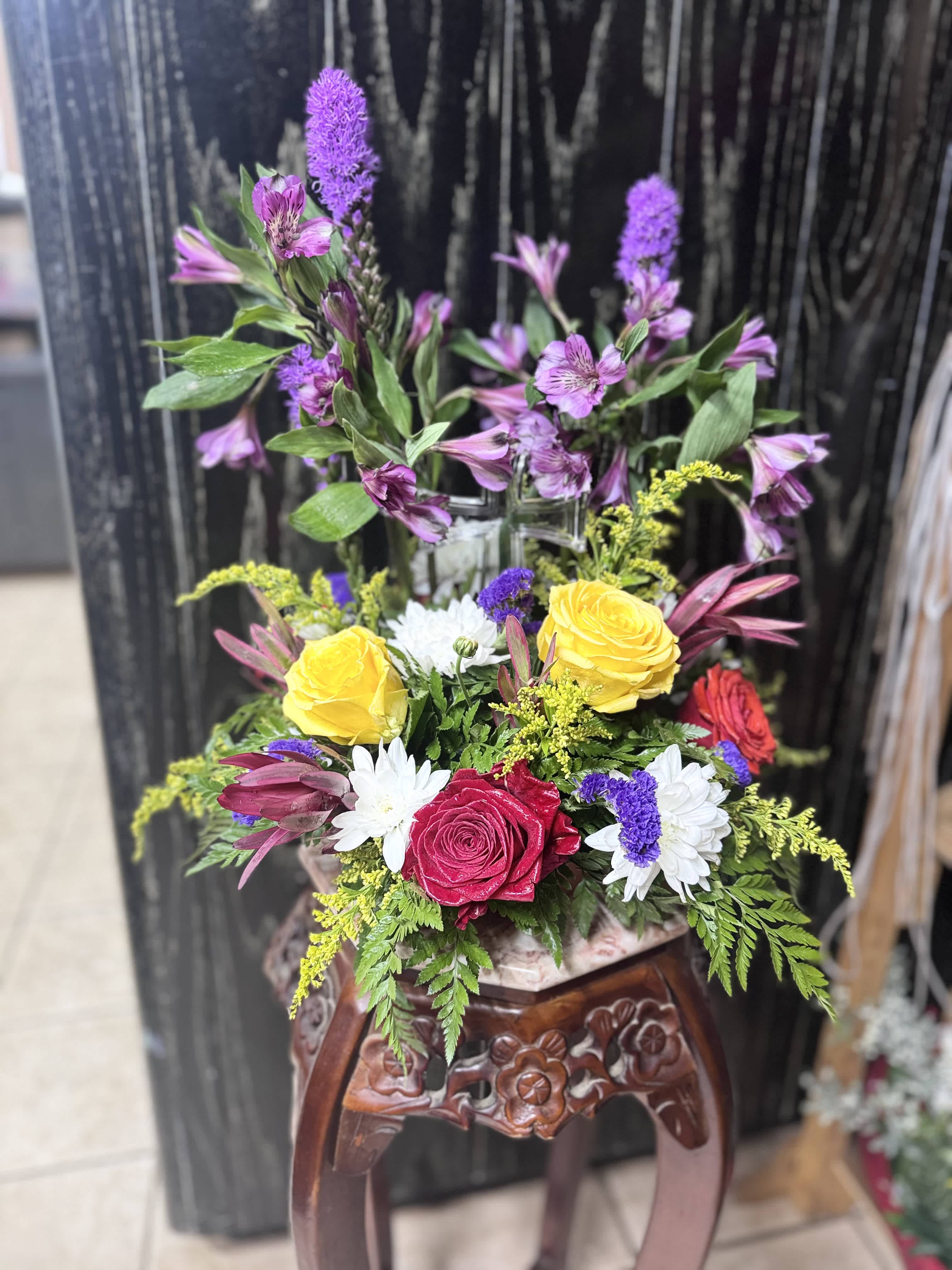 Mixed bouquet with yellow and red roses, white daisies, and purple flowers in a vase