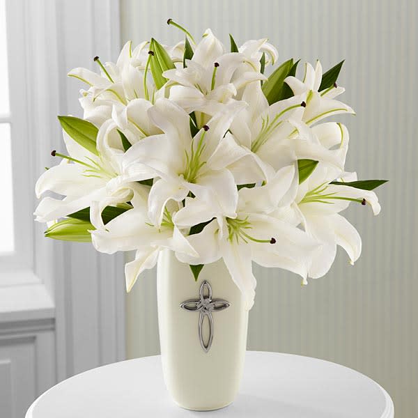 White lilies arranged in a cream vase with a silver cross