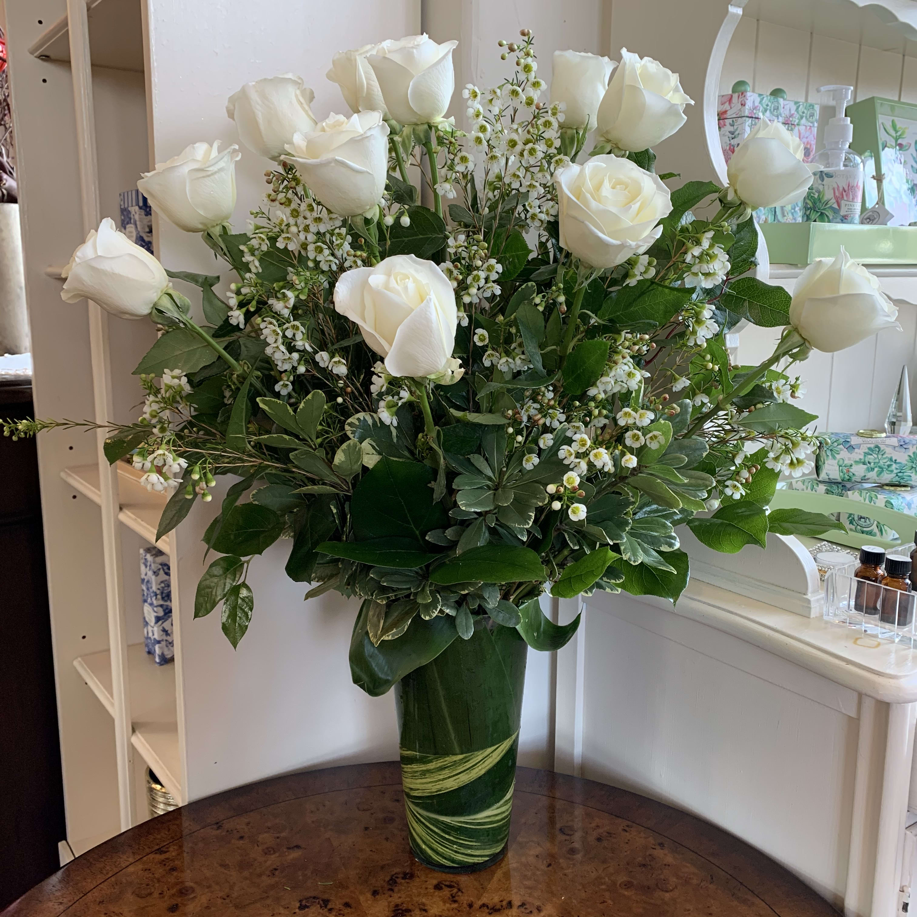 White roses and small white filler flowers in a green glass vase.