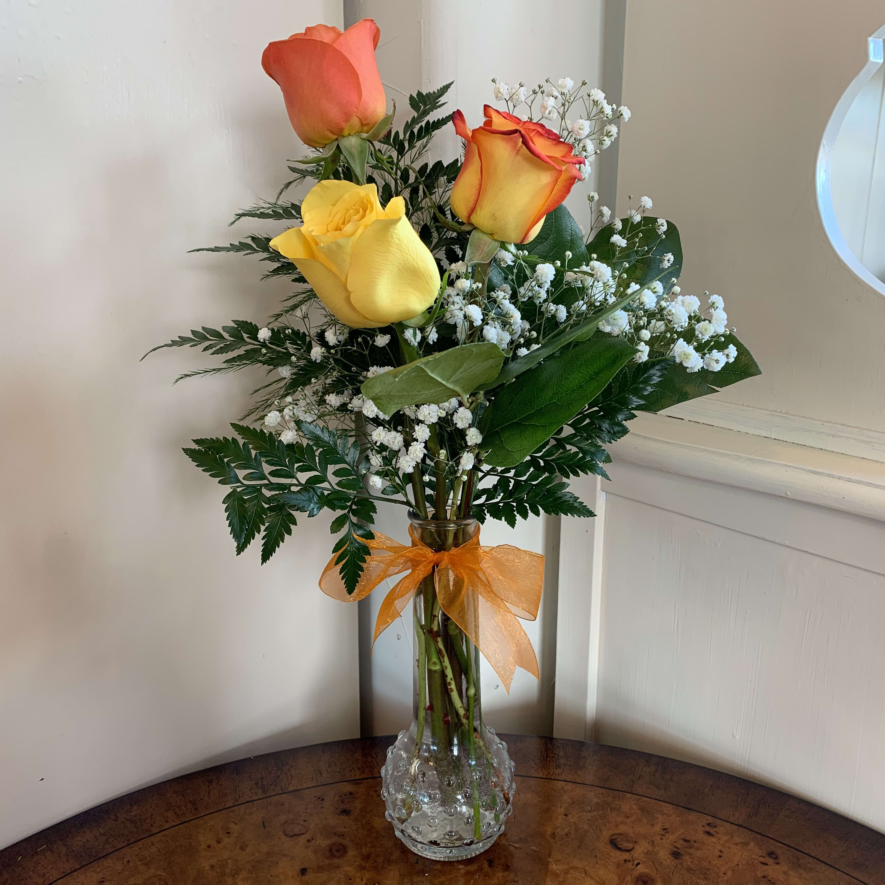 Three roses in a clear vase with baby's breath and an orange ribbon