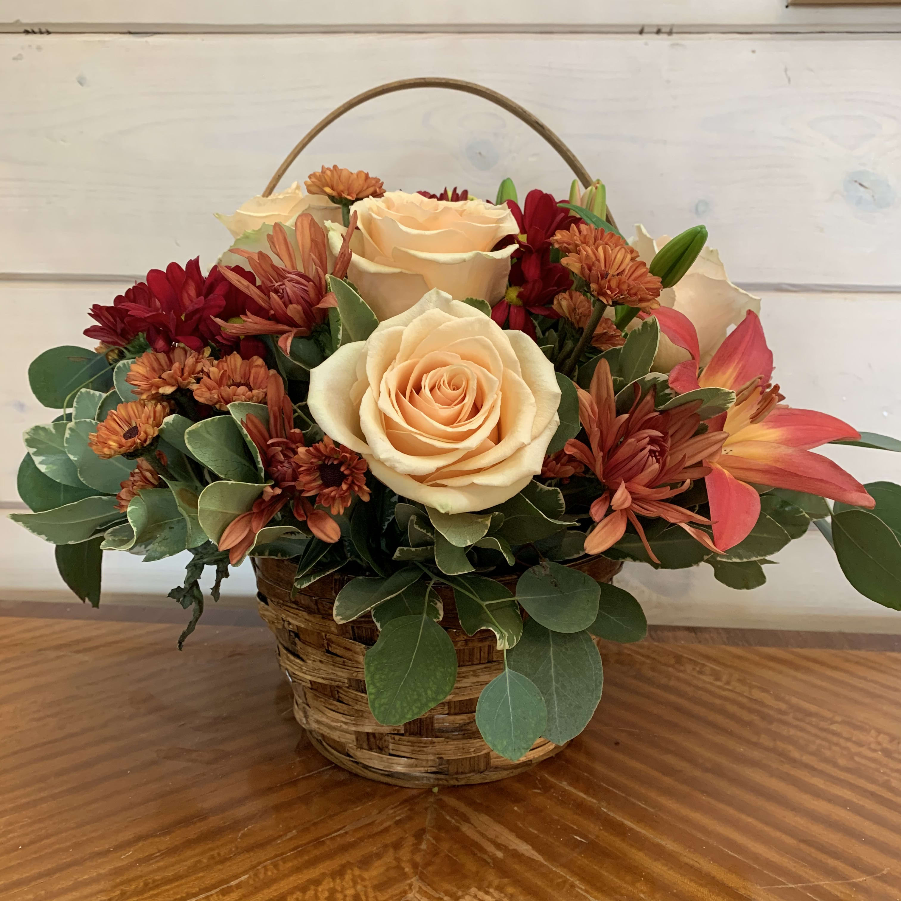 Peach roses and orange mums arranged in a wicker basket