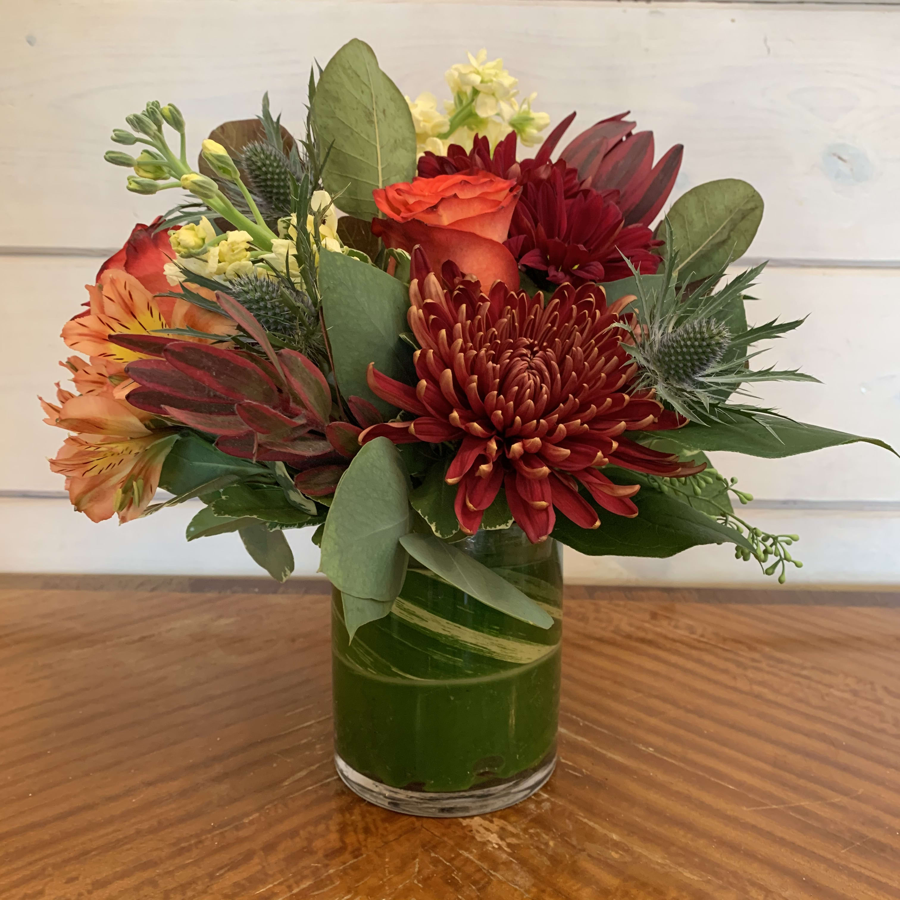Mixed bouquet of red, orange, and yellow flowers in a glass vase