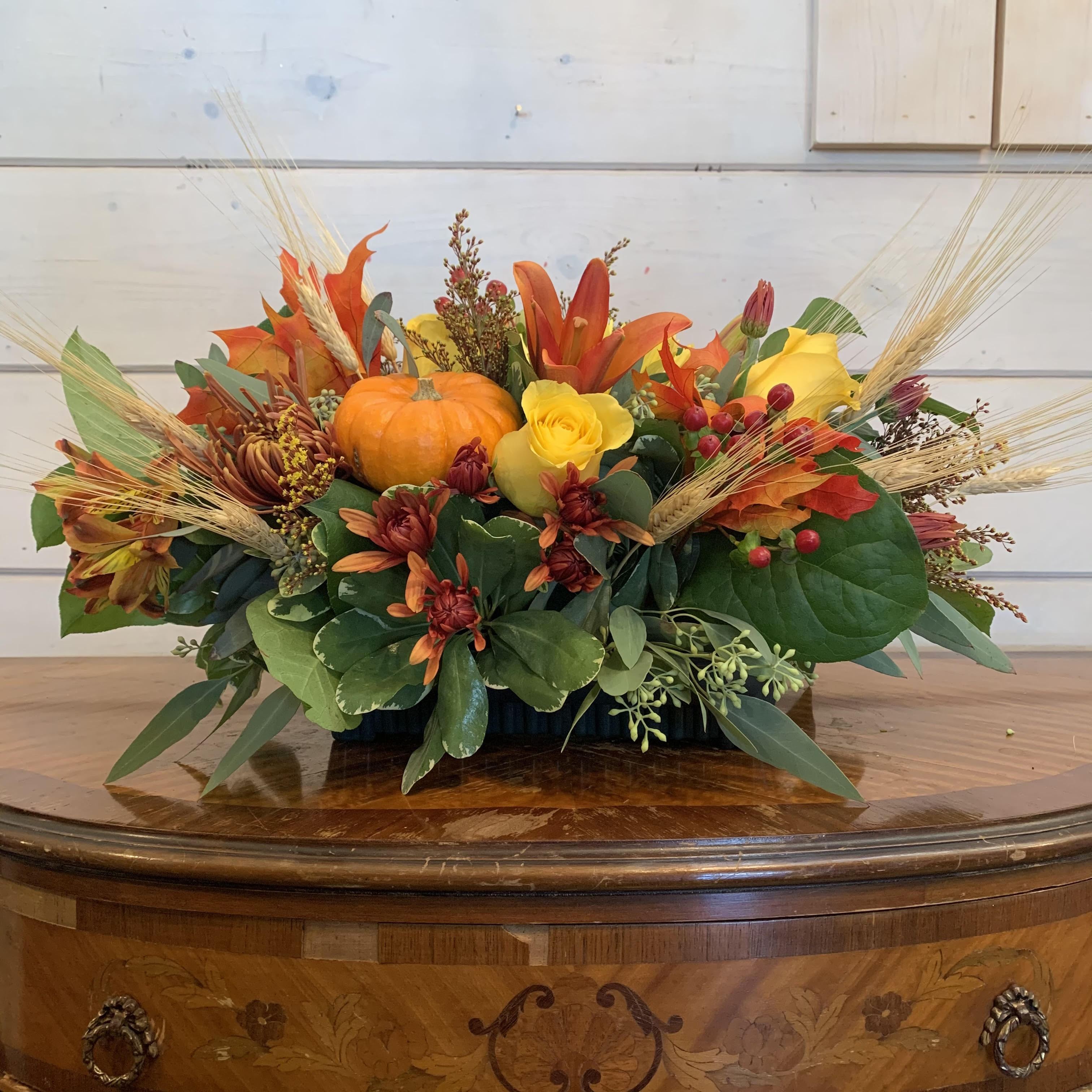 Autumn floral arrangement with pumpkins and orange-yellow flowers in a low container