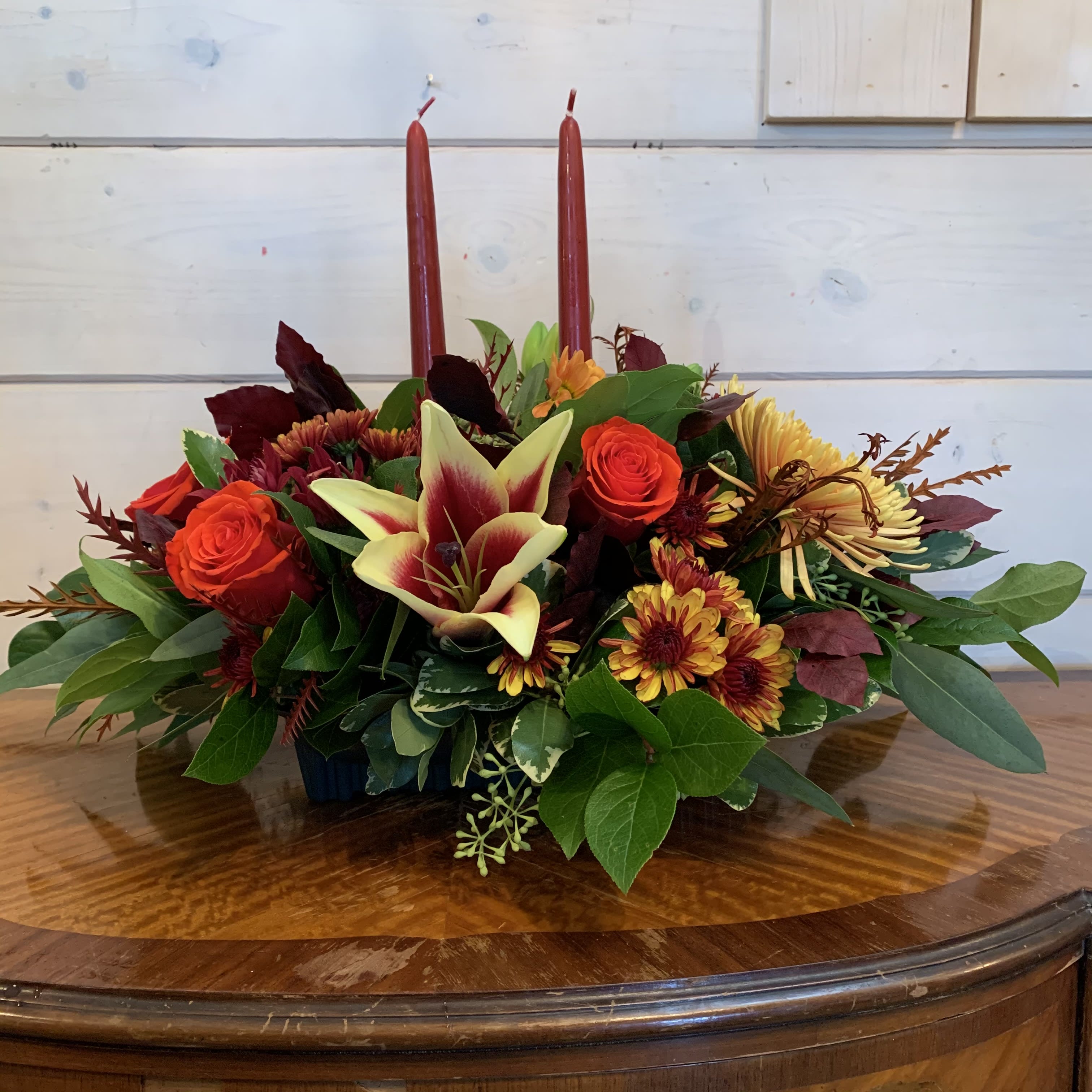 Low floral centerpiece with red candles and orange roses in a dark container