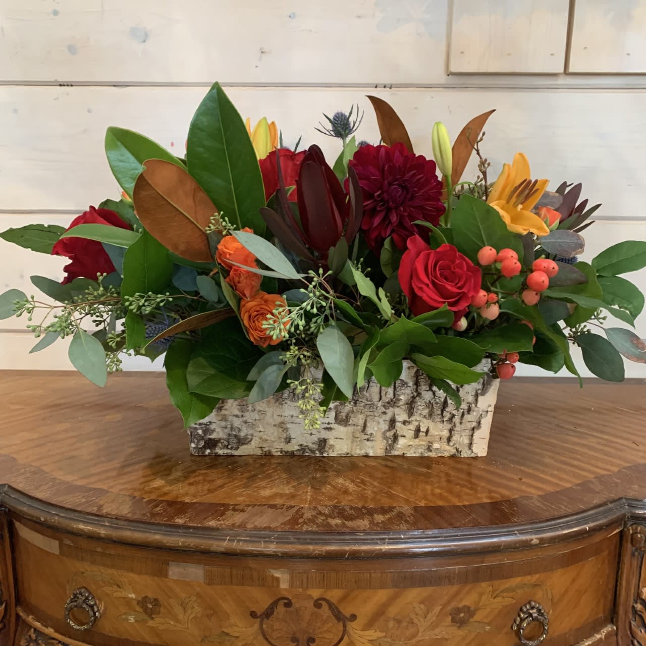 Mixed floral arrangement in a birch bark container with red, orange, and yellow blooms