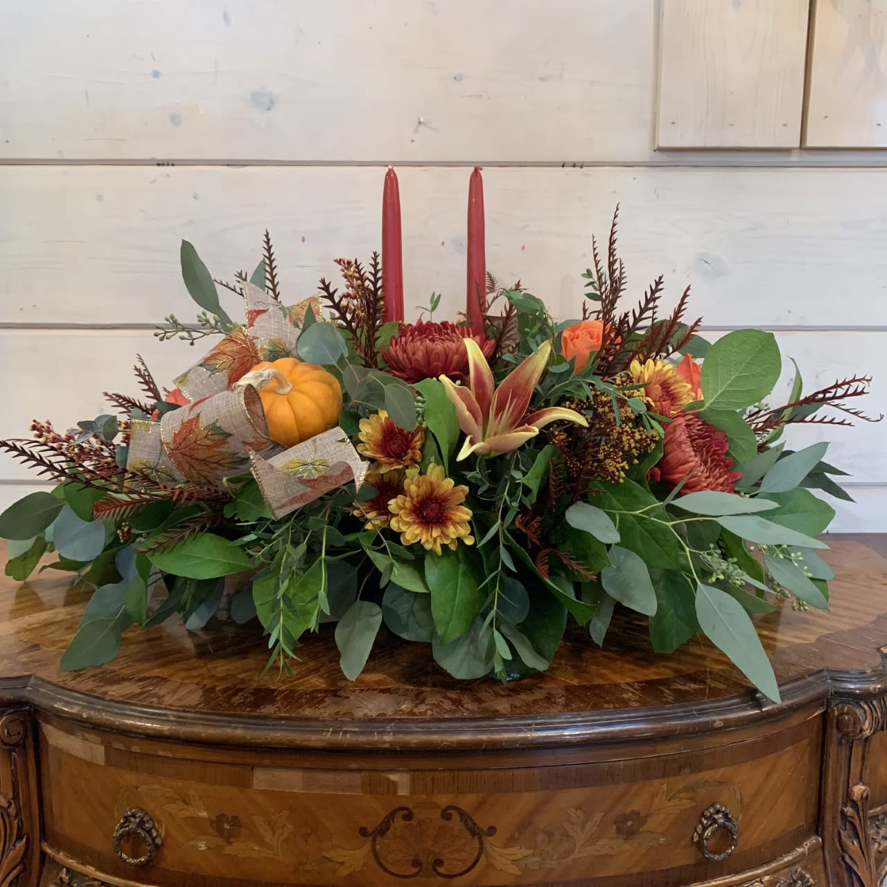 Autumn centerpiece with red candles, orange flowers, and a small pumpkin