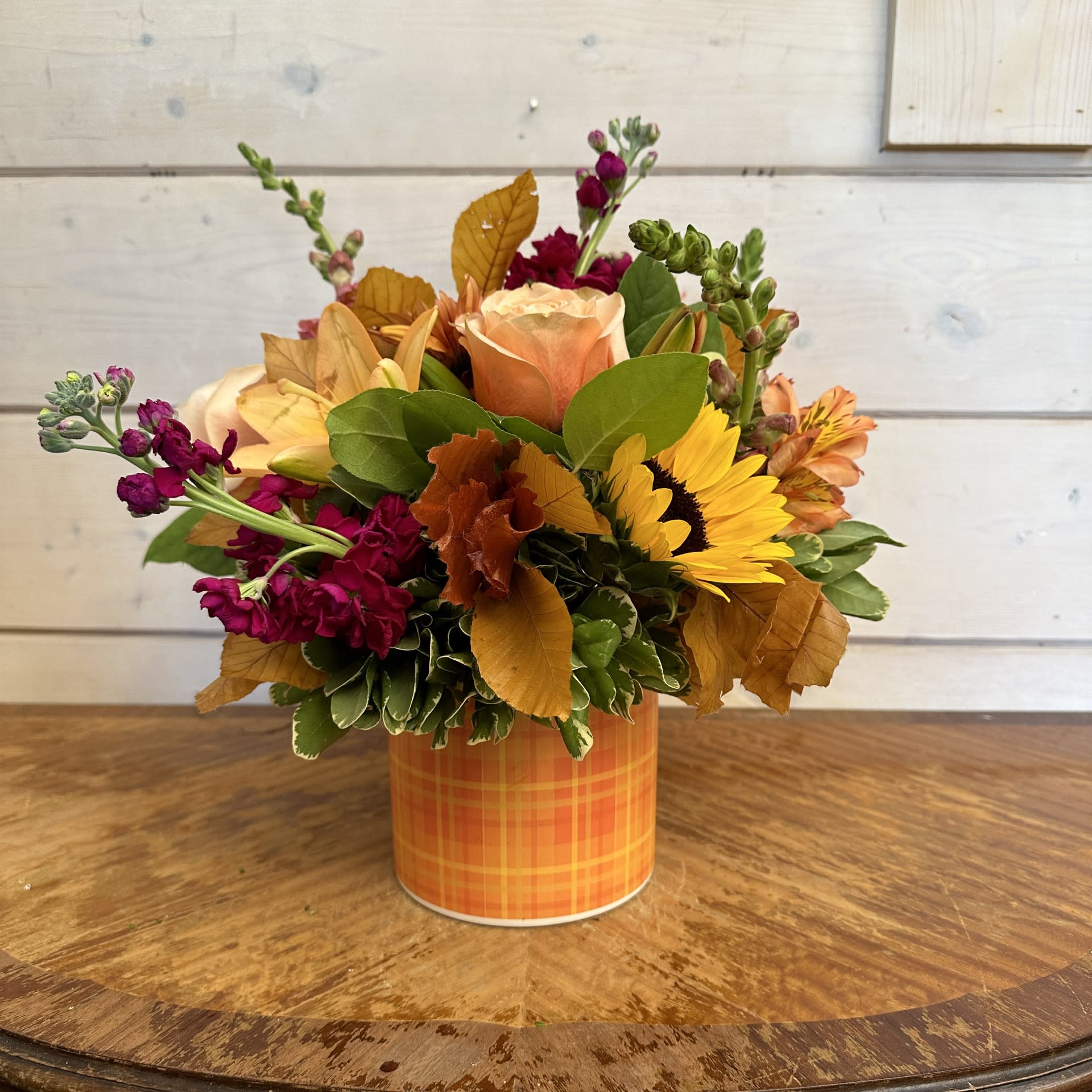 Autumn flower arrangement in an orange plaid container with yellow and peach blooms