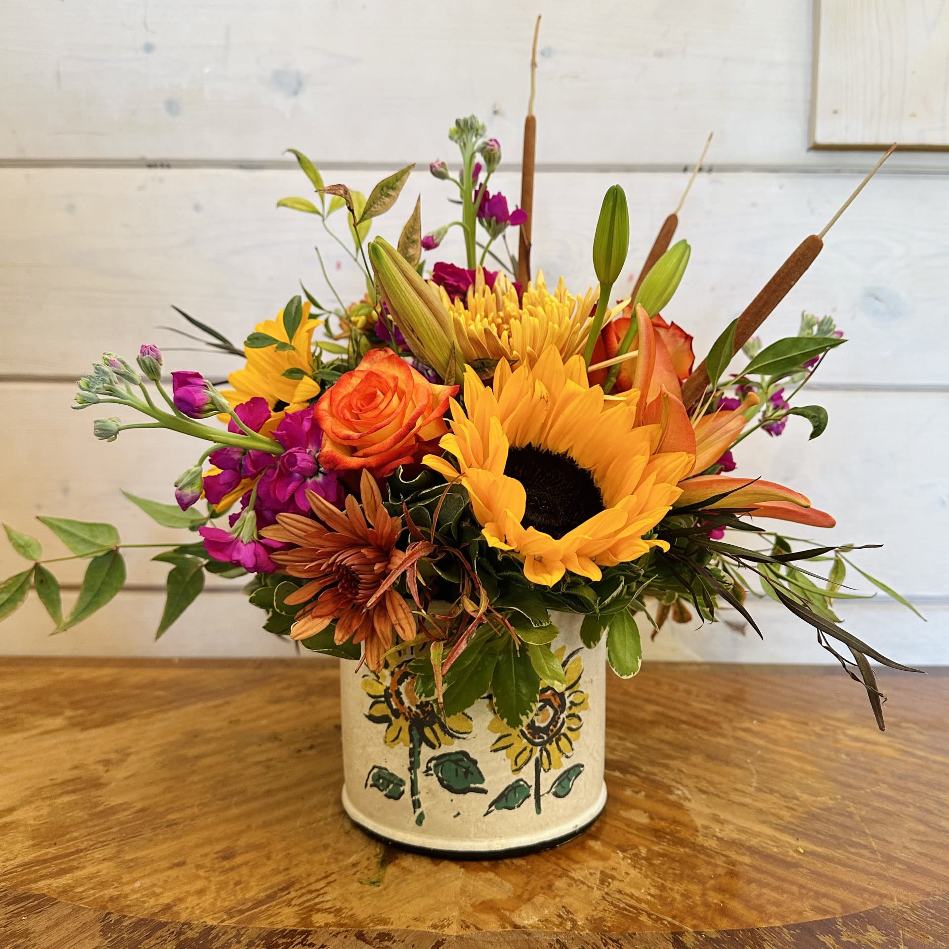 Mixed bouquet with sunflowers, roses, and purple blooms in a painted tin container