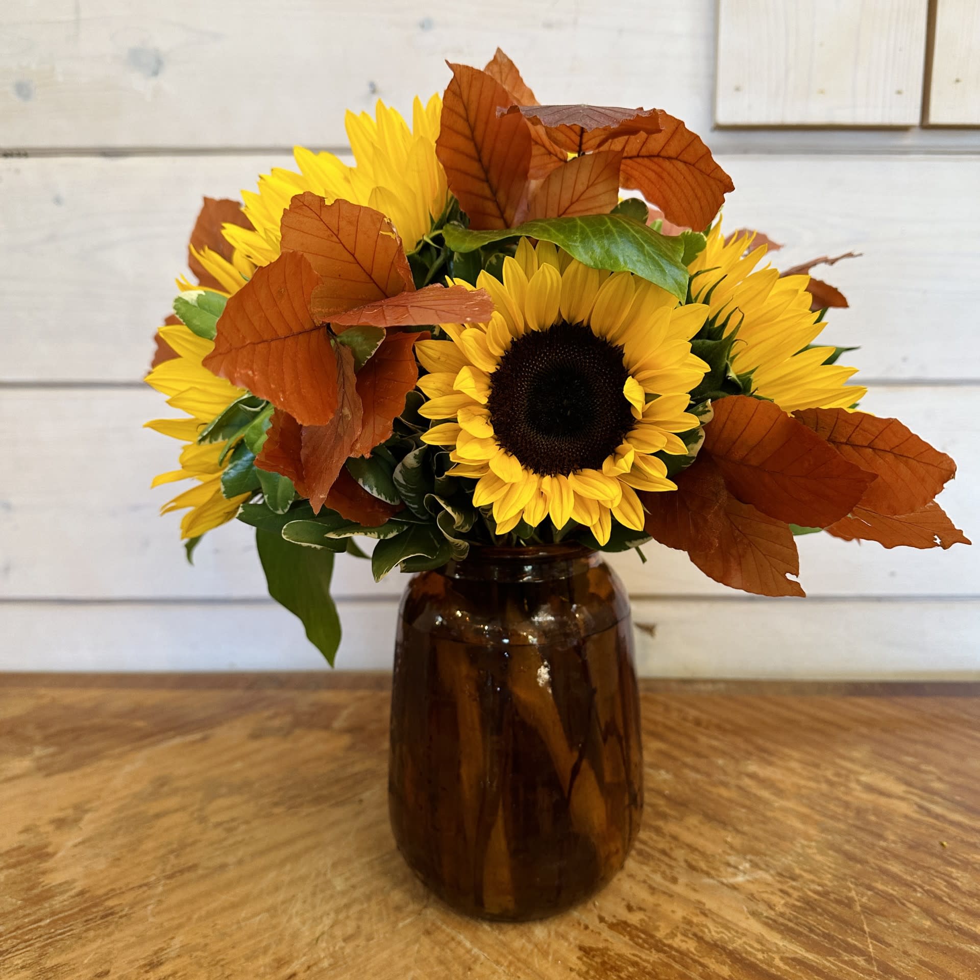 Sunflowers arranged in a brown glass vase with autumn leaves