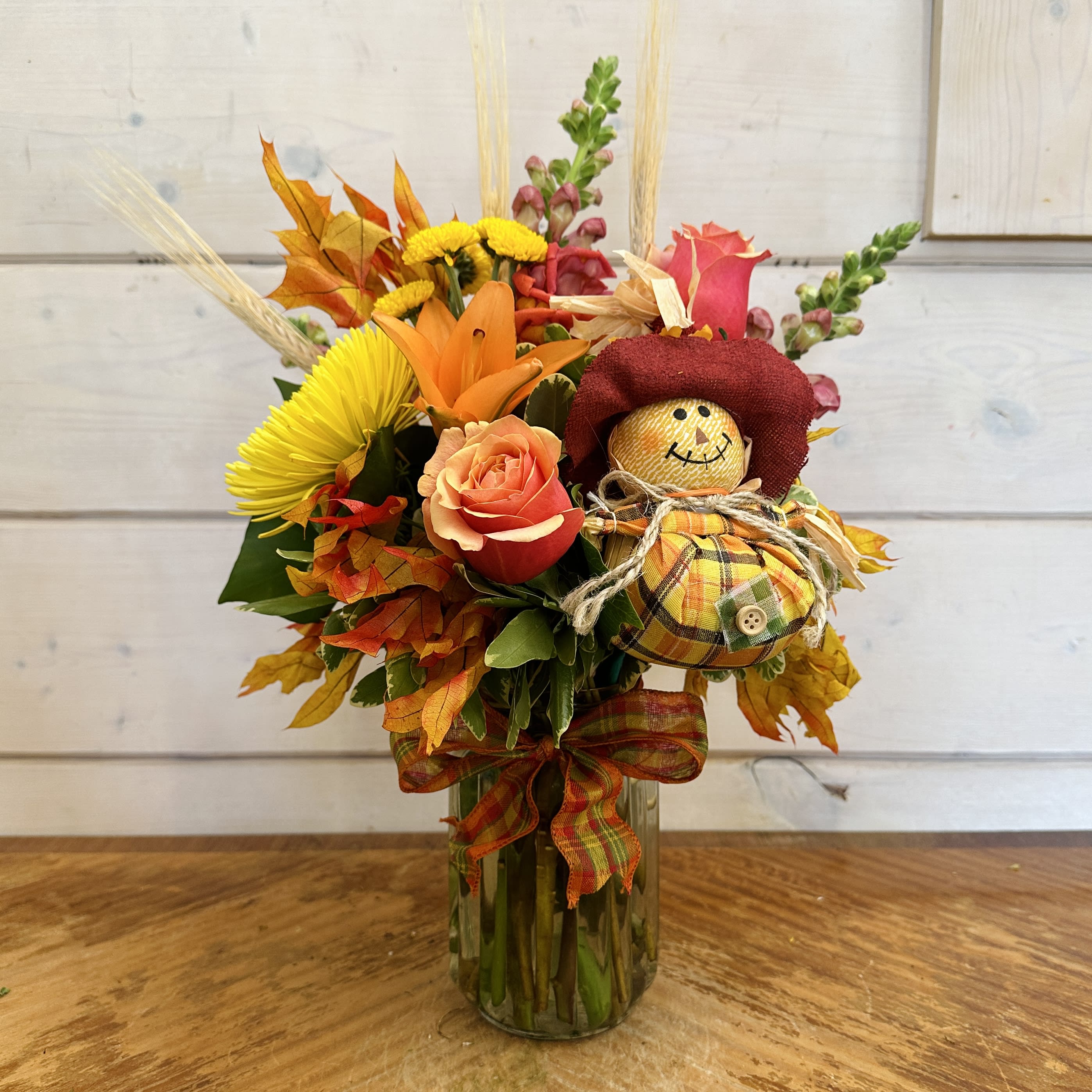 Fall bouquet in a glass vase with a small scarecrow decoration