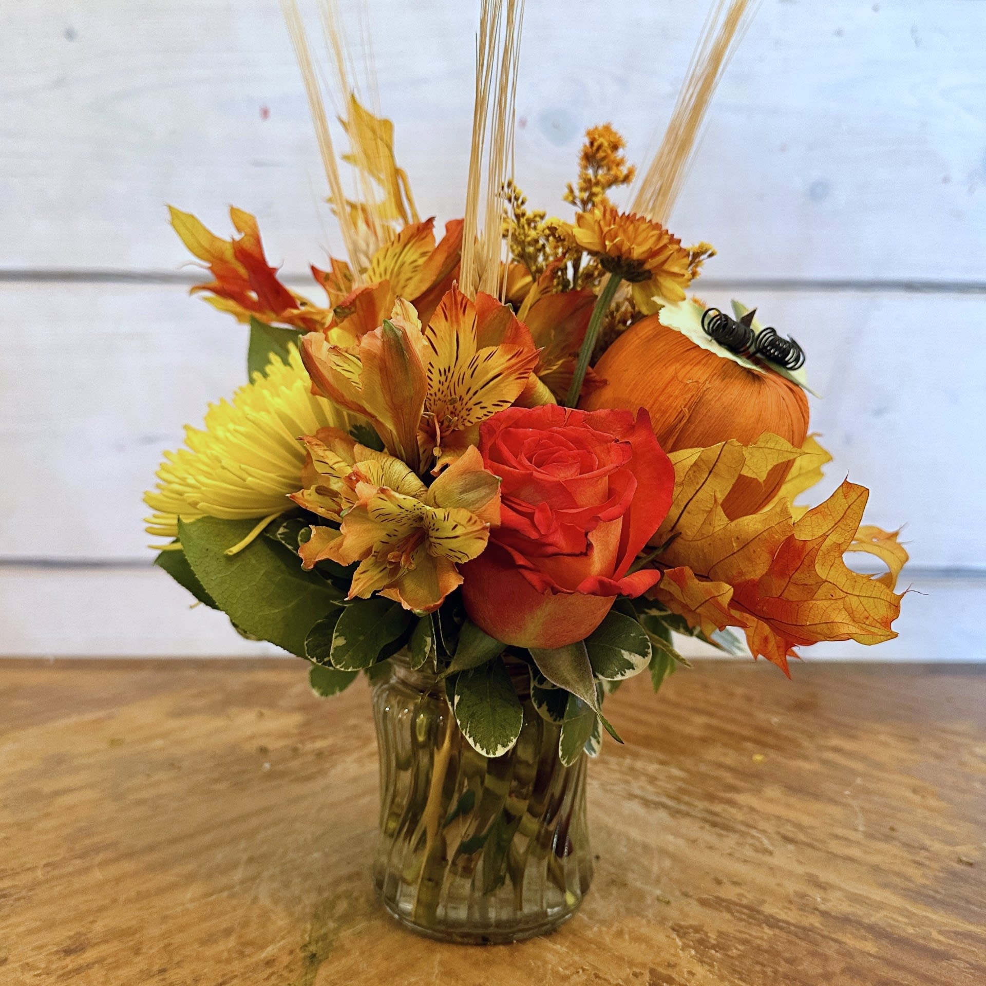 Autumn floral arrangement with orange roses and yellow blooms in a glass vase