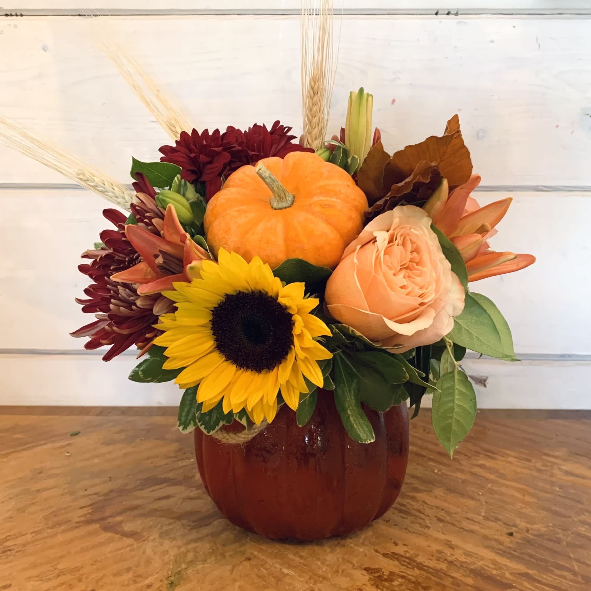 Pumpkin centerpiece with sunflowers, peach roses, and burgundy mums in a vase