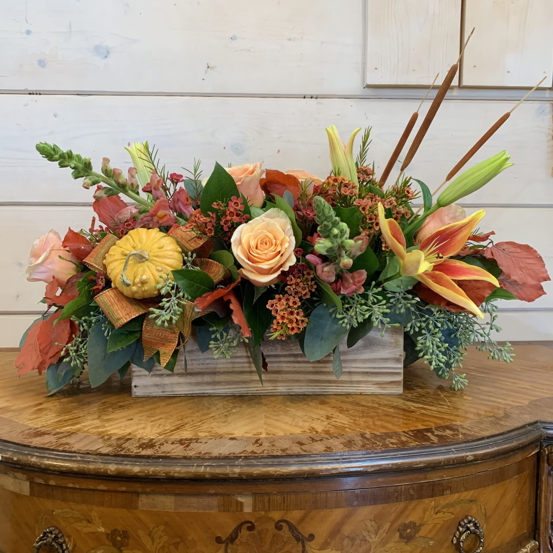 Autumn floral arrangement in a wooden box with roses, lilies, and a small pumpkin