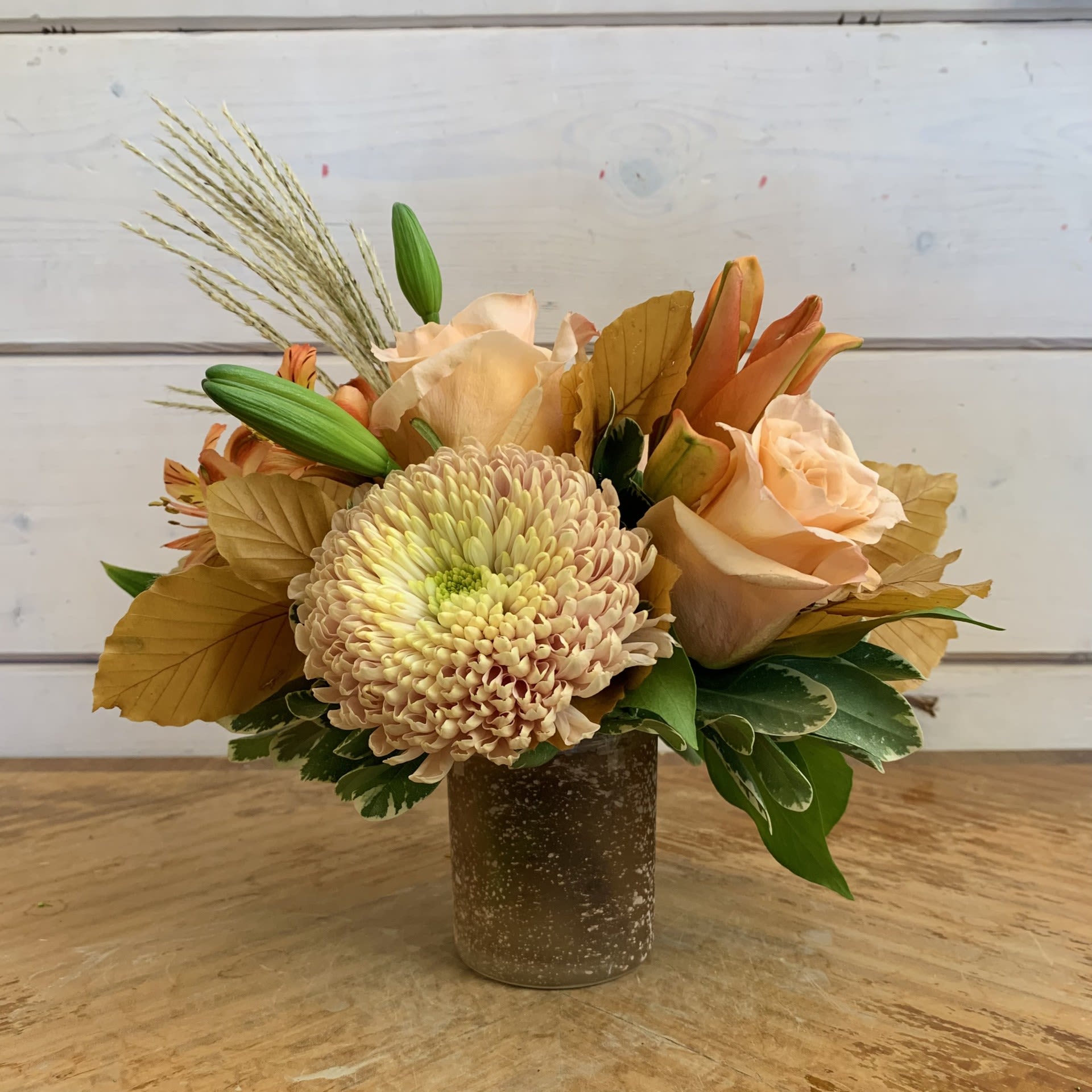 Peach roses and a chrysanthemum in a brown vase with autumn leaves