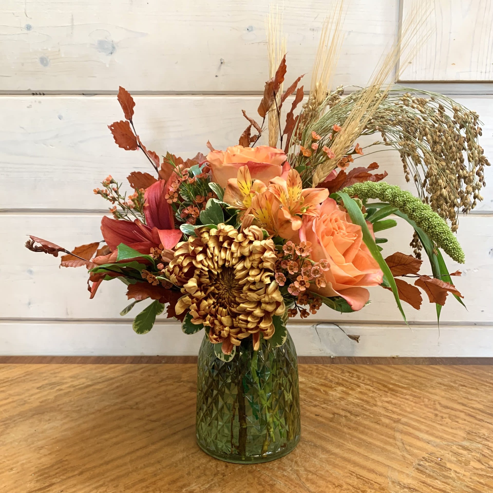 Autumn bouquet of orange and rust flowers in a green glass vase