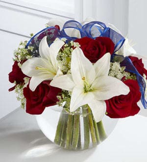 Red roses and white lilies in a clear glass vase with blue ribbon