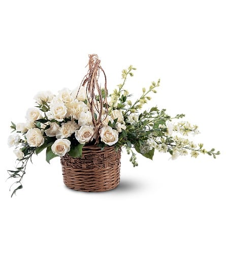 White rose arrangement in a wicker basket with trailing greenery