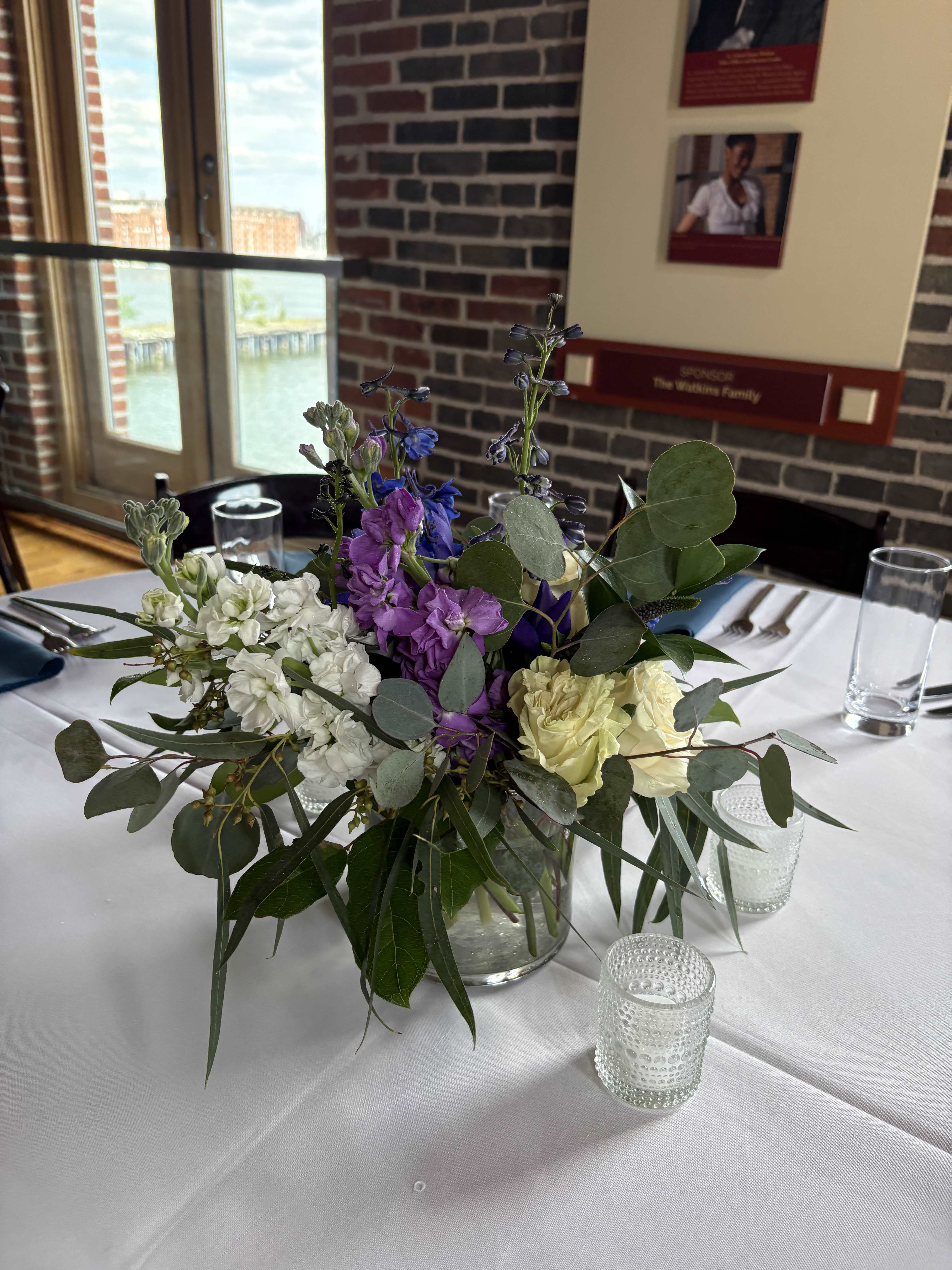 Mixed purple, white, and pale yellow flowers in a clear glass vase on a table