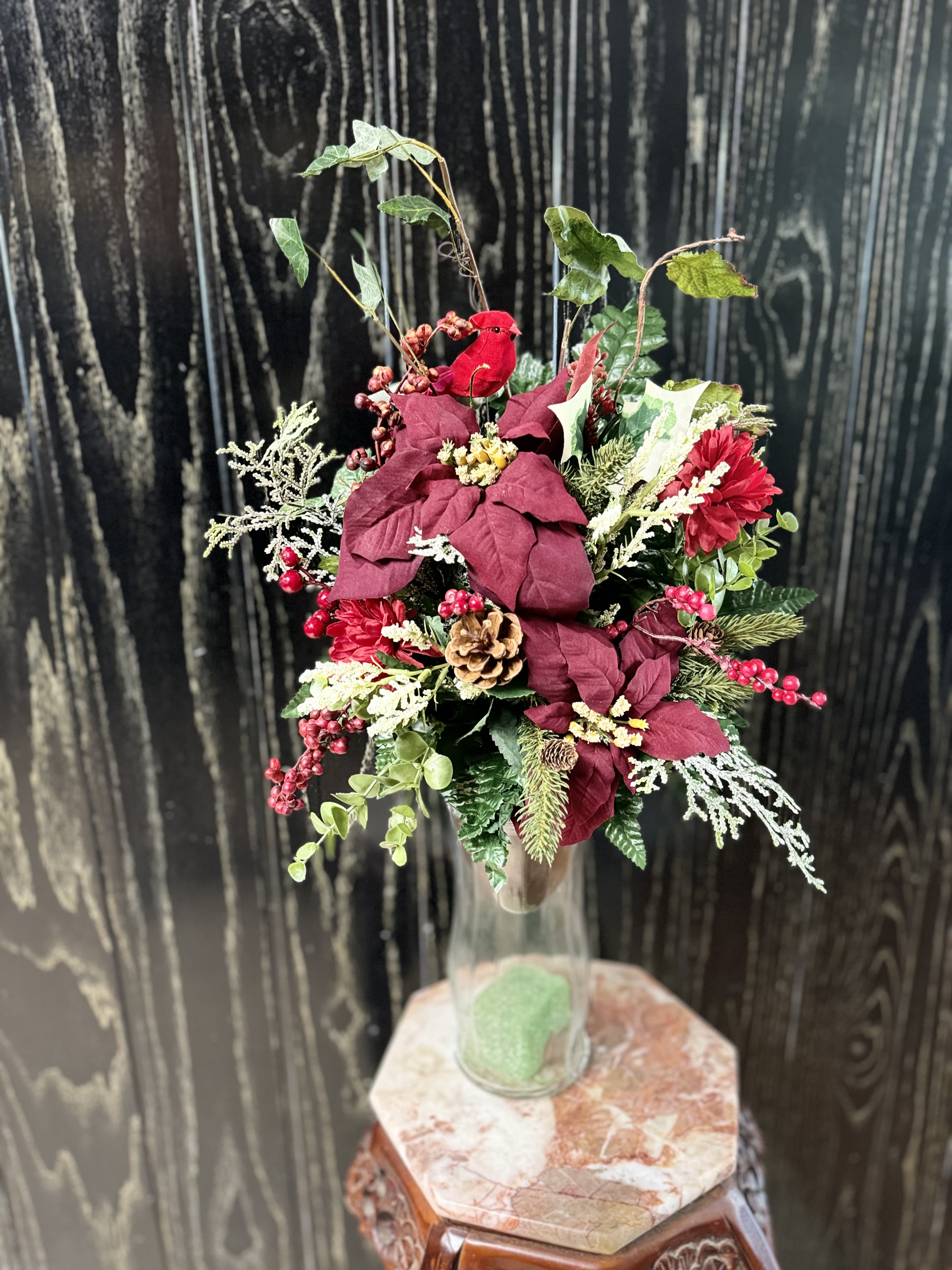 Holiday floral arrangement in a clear glass vase with red blooms and berries