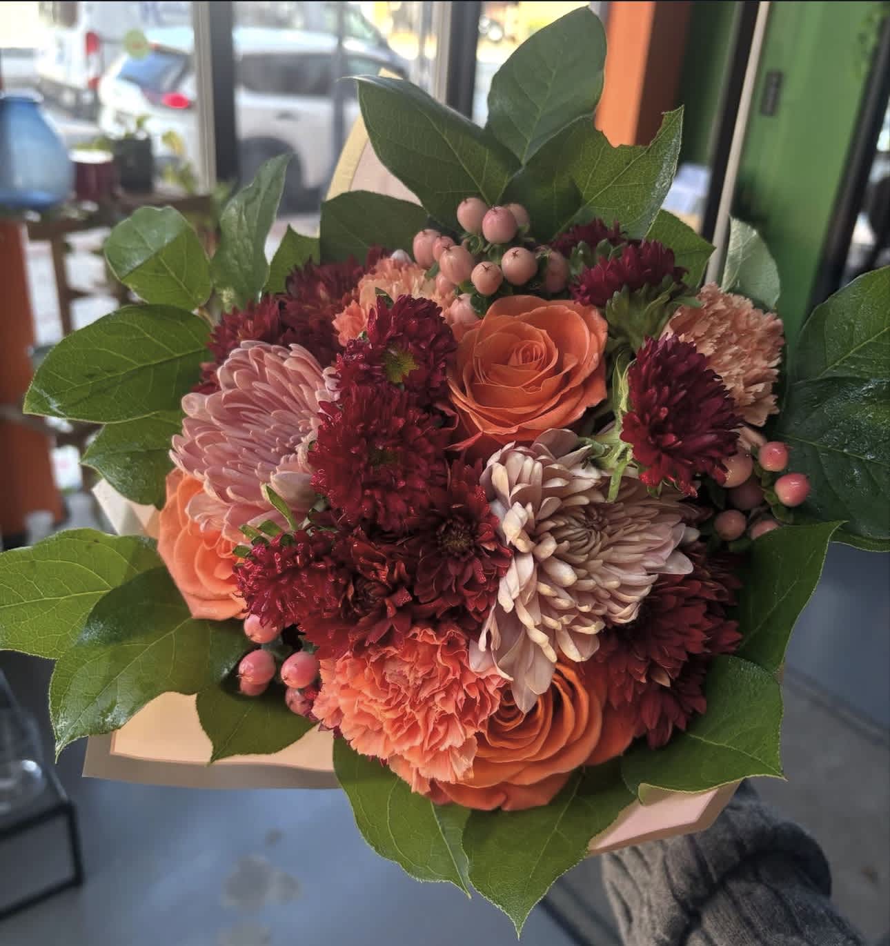 Handheld bouquet of orange and burgundy flowers with large green leaves