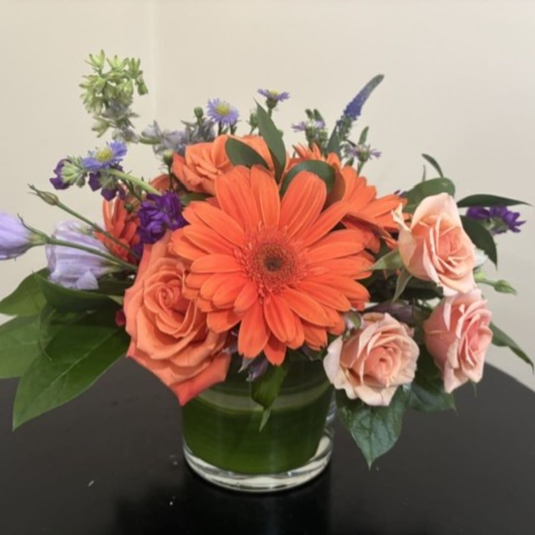 Orange gerbera daisies and peach roses in a glass vase