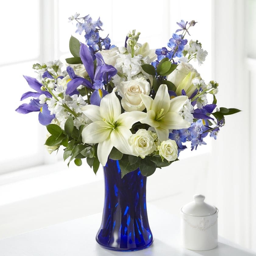 White lilies, roses, and blue-purple flowers in a cobalt vase