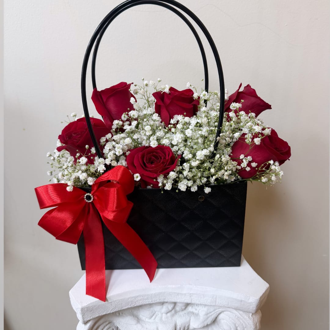 Red roses in a black handled gift bag with a red bow