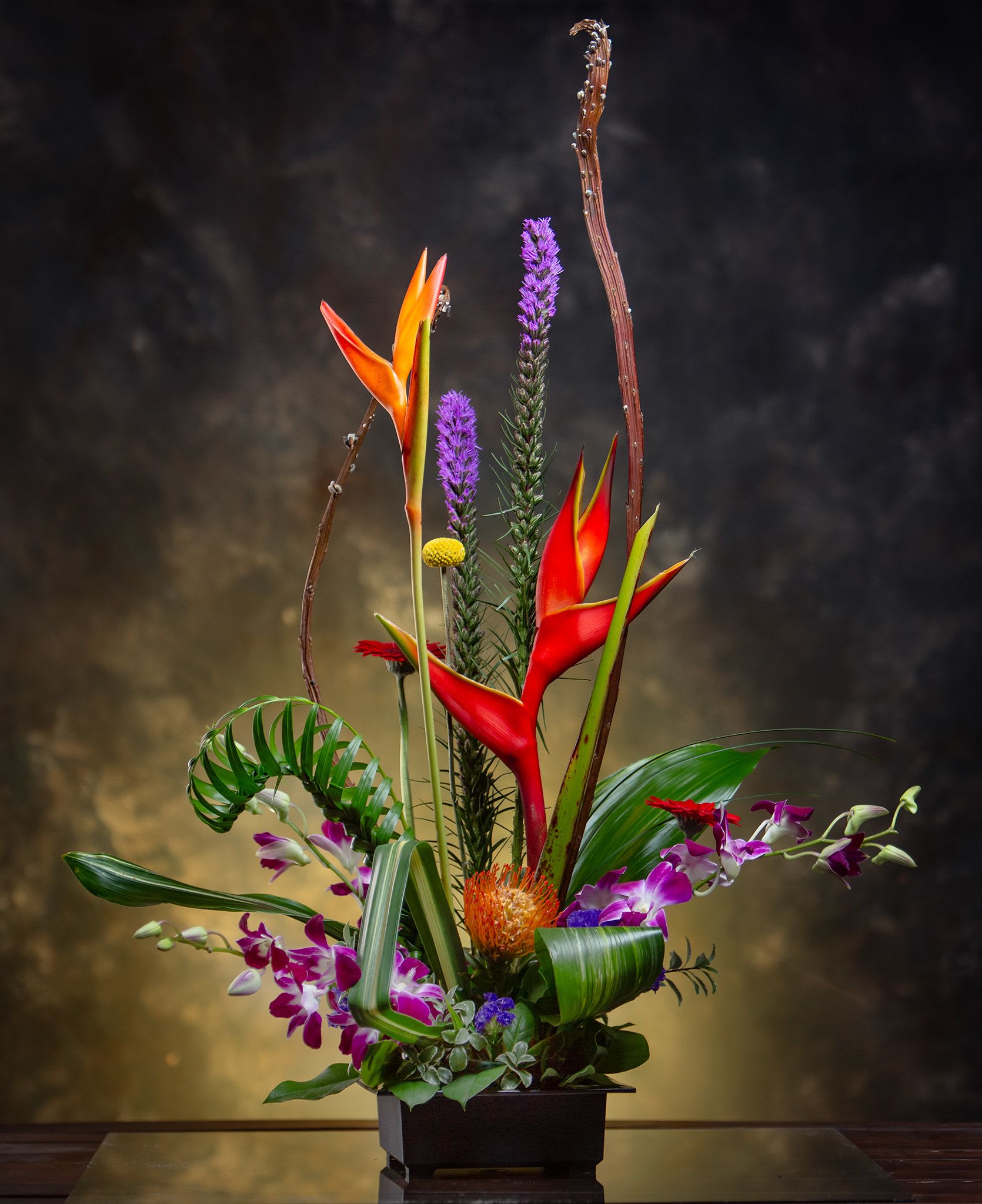 Tropical floral arrangement with red heliconia and purple orchids in a black container