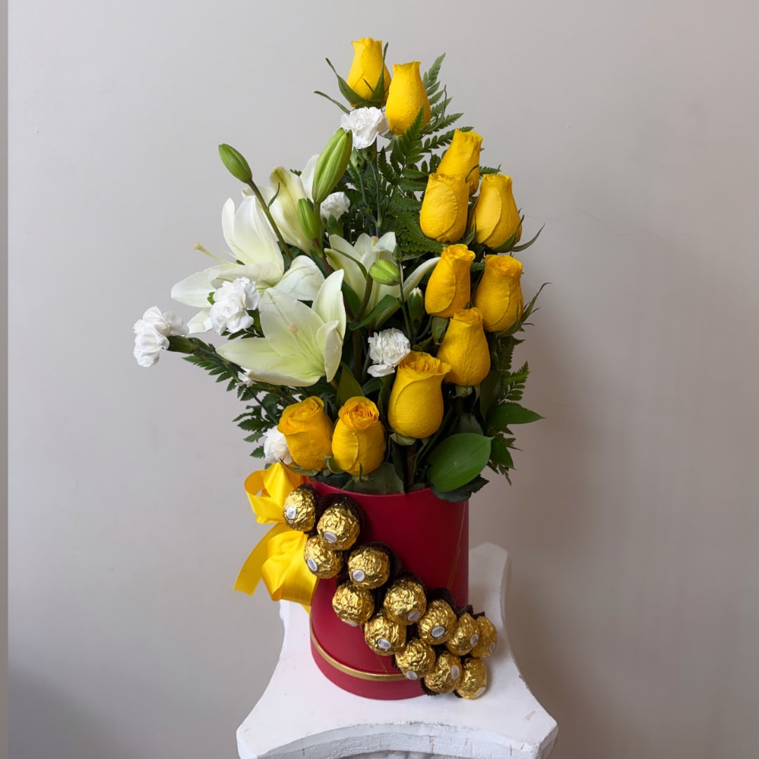 Yellow roses and white lilies in a red hatbox with gold chocolates