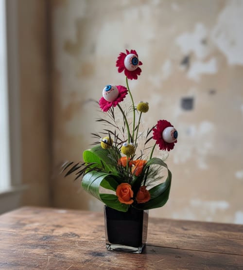 Small floral arrangement with orange roses and pink daisy-like blooms in a black vase